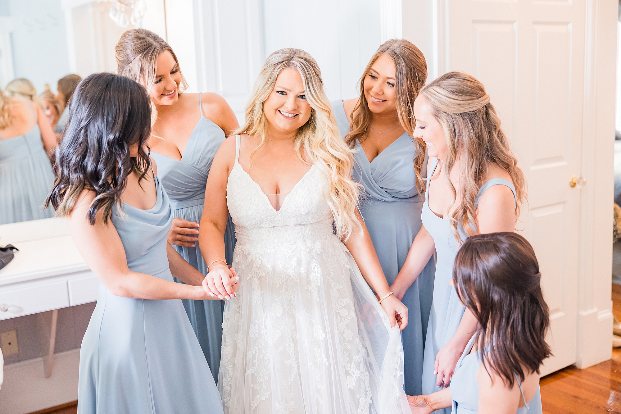 bridesmaids in blue gowns hold bride's hand