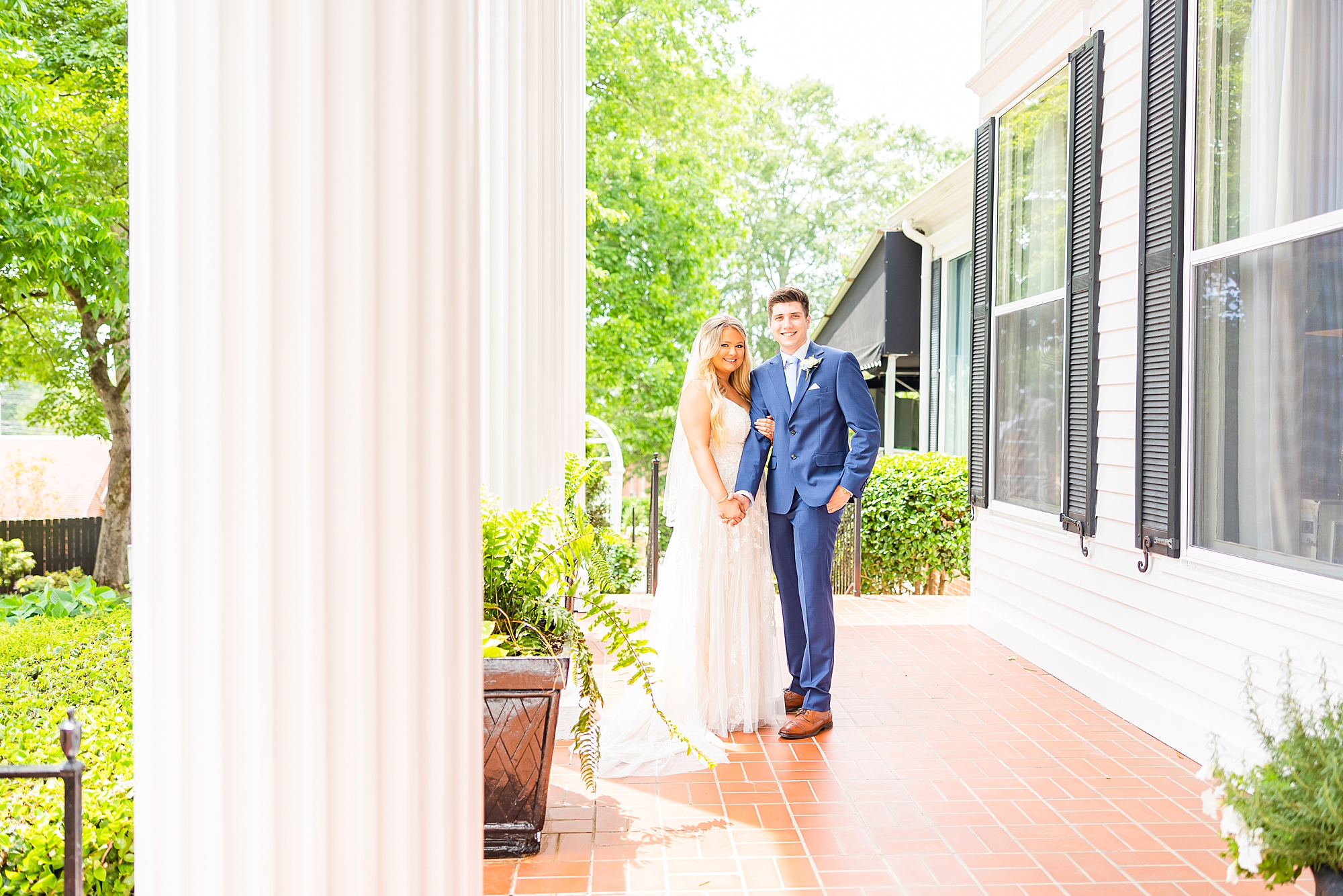 newlyweds stand on veranda at Victoria Belle Mansion