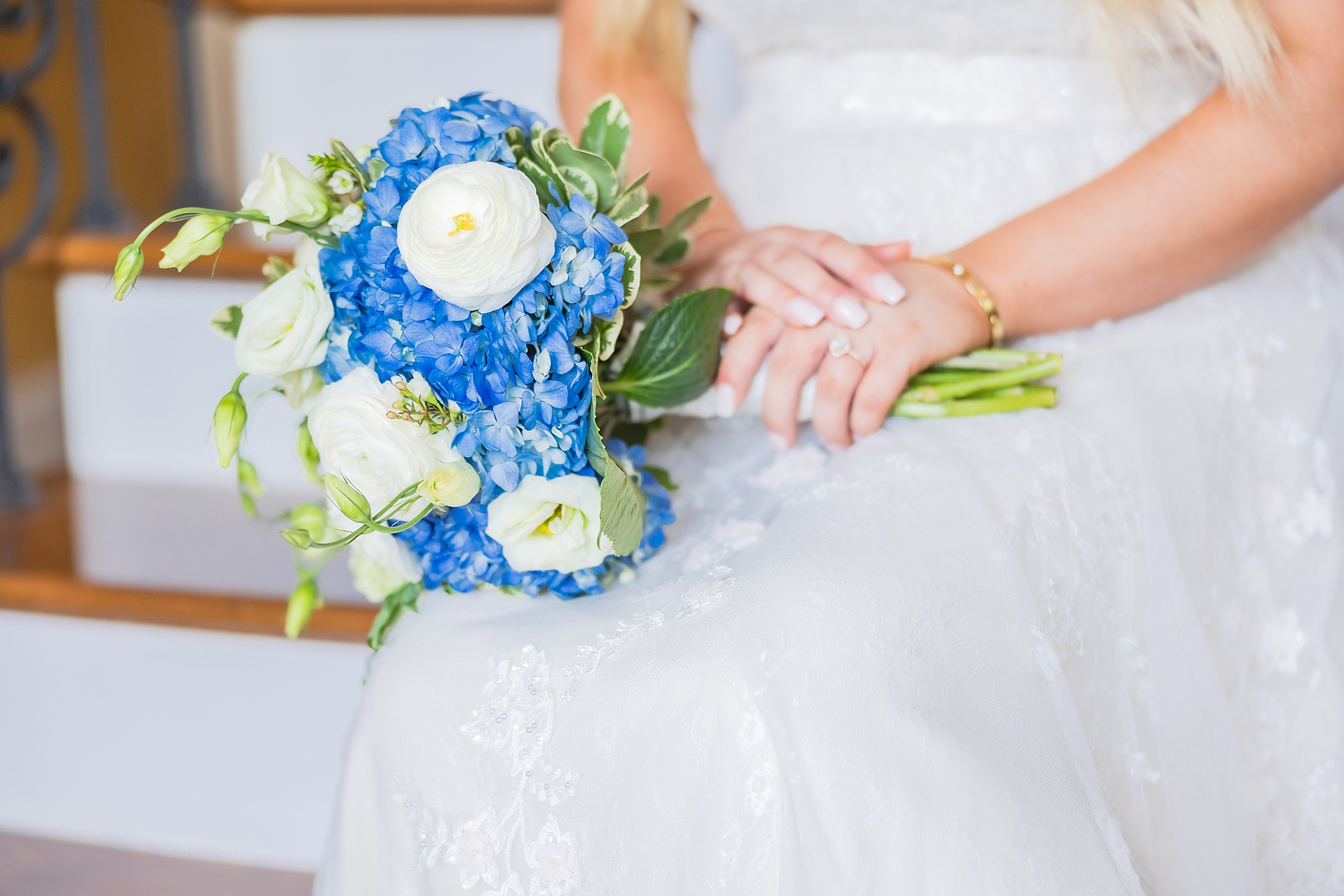 bride holds bouquet of blue and white flowers on lap