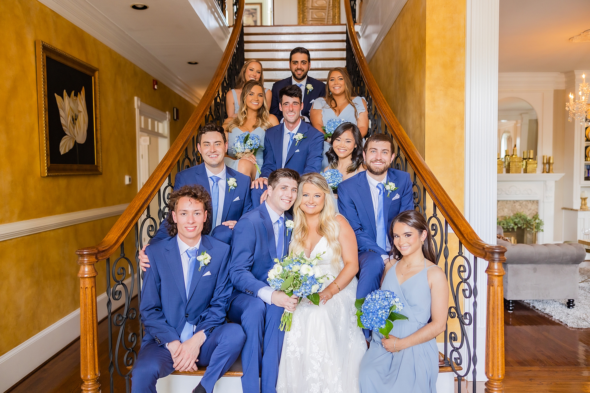 bride and groom sit on staircase with wedding party