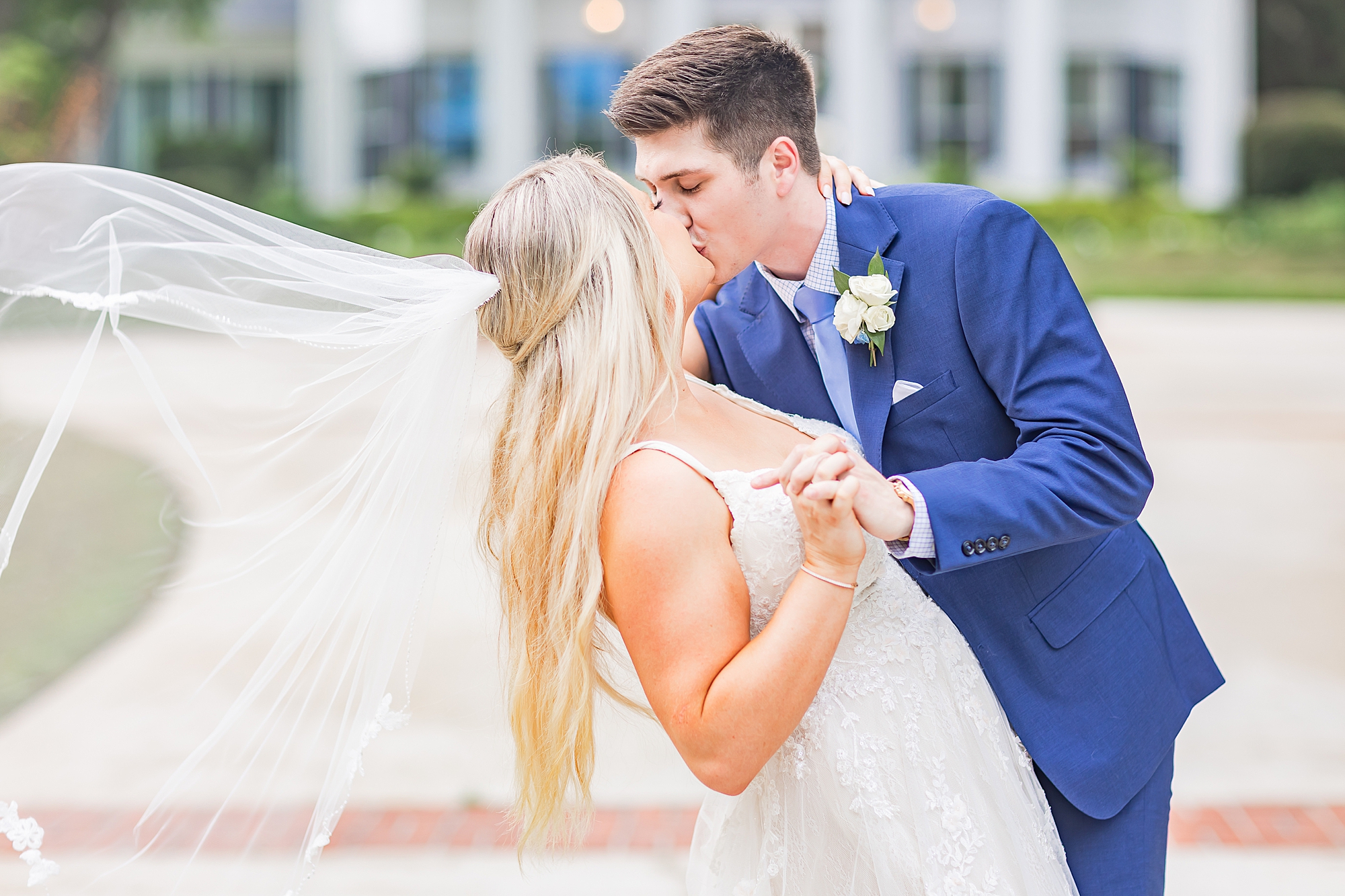 groom kisses bride with veil floating behind her