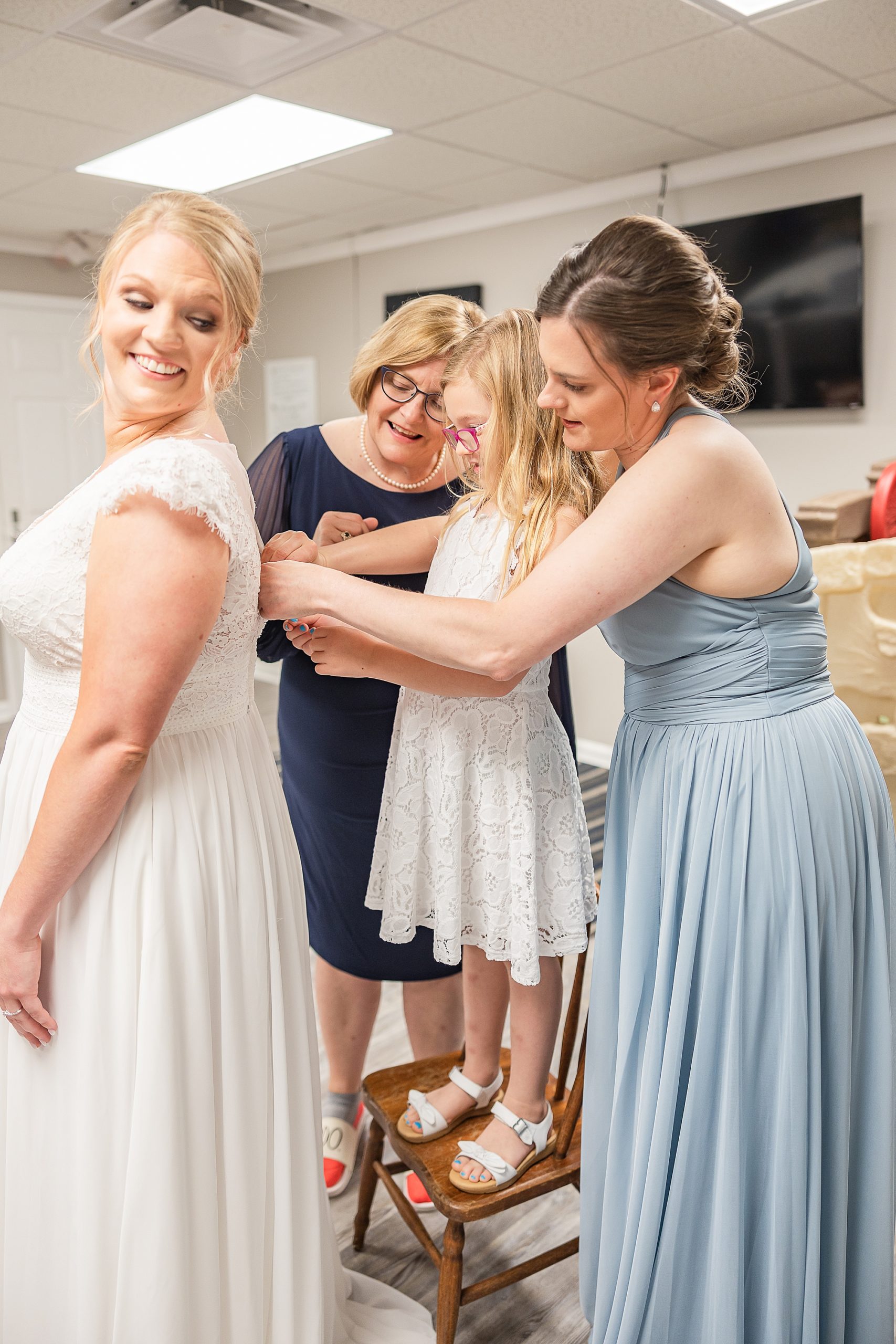 bridesmaid in blue gown helps bride with gown