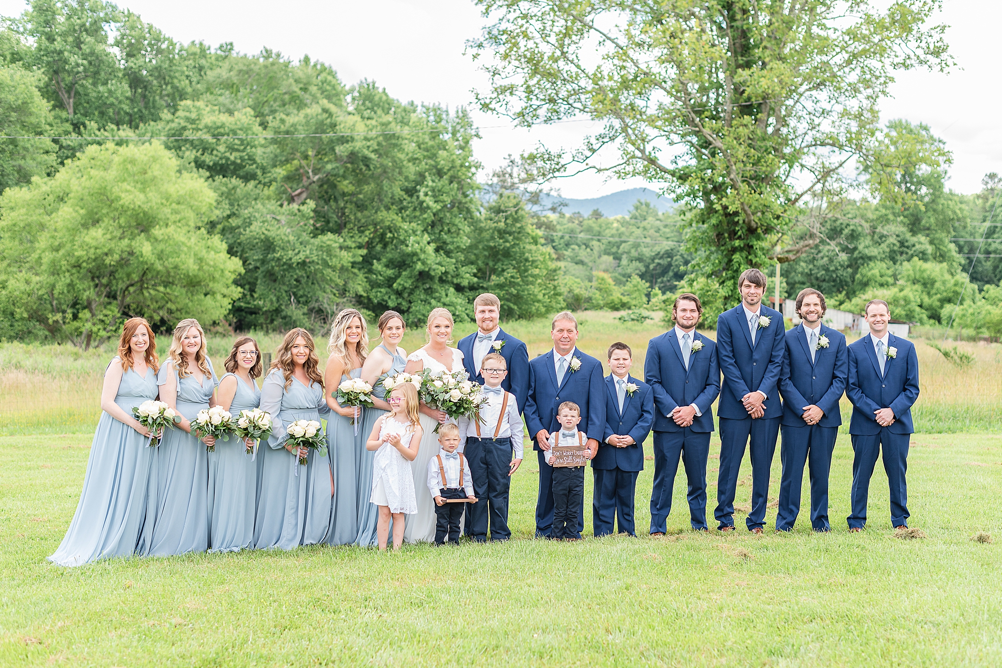 bride and groom stand with wedding party in light blue and navy suits