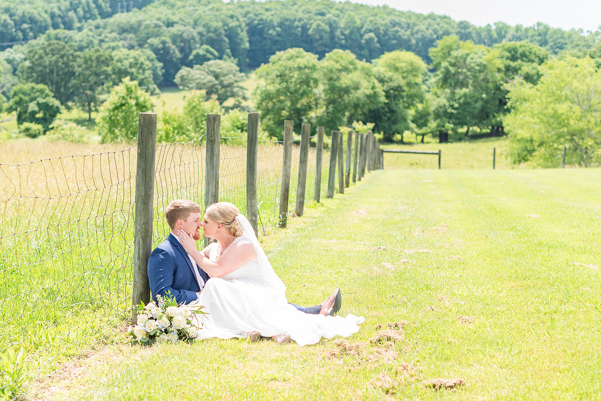 couple sits in field against wooden posts during Blairsville GA wedding photos