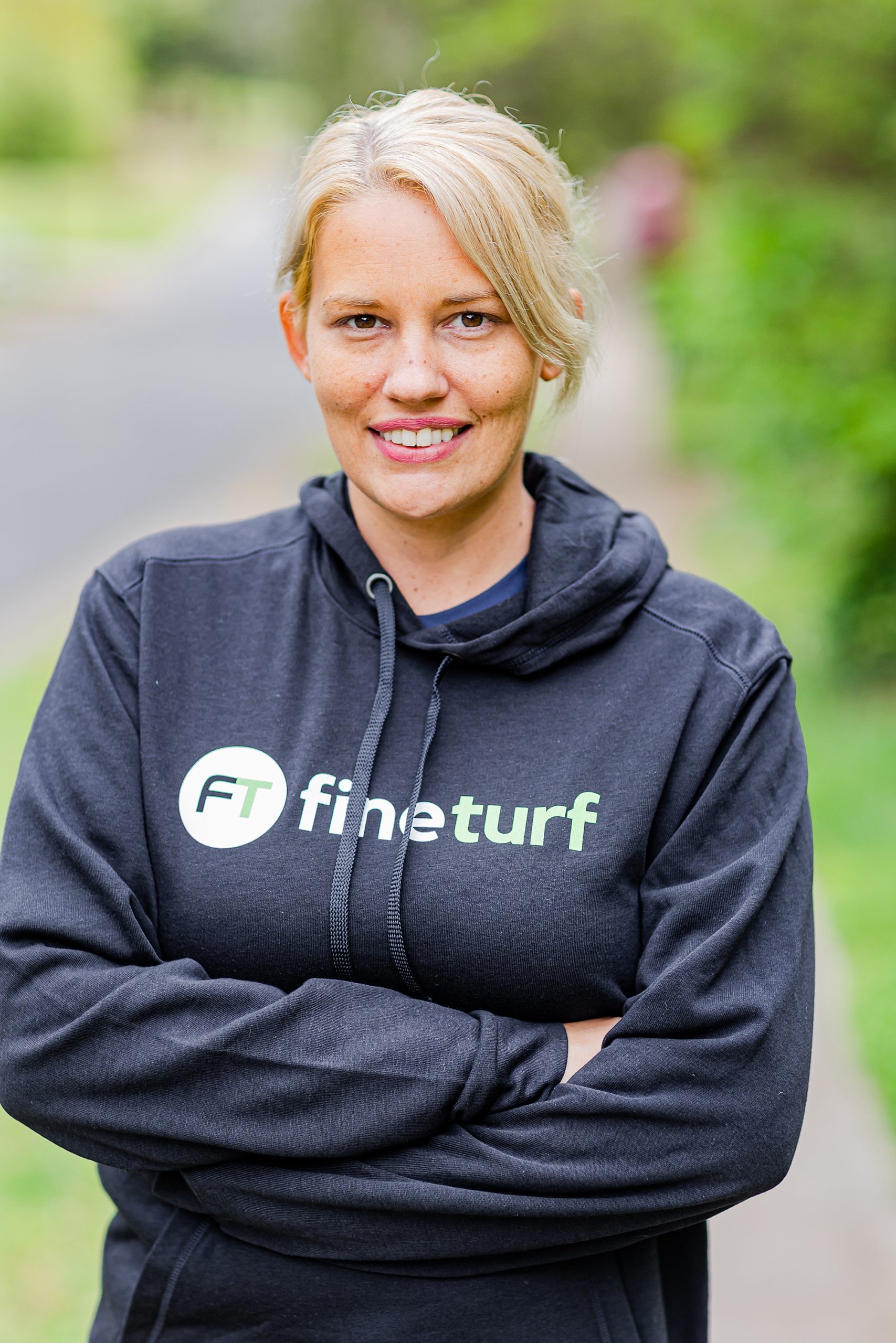 woman stands with arms crossed in Fine Turf sweatshirt