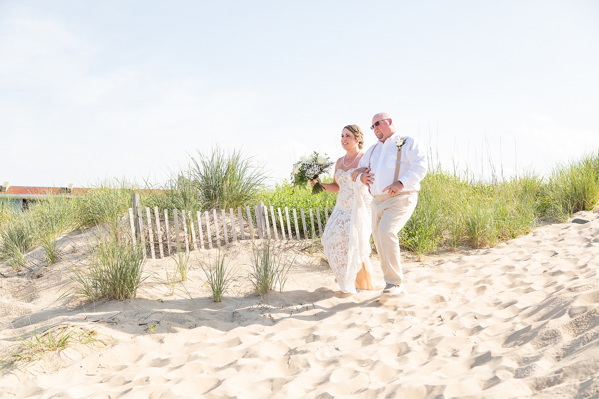 bride walks down hill with dad for beach wedding ceremony