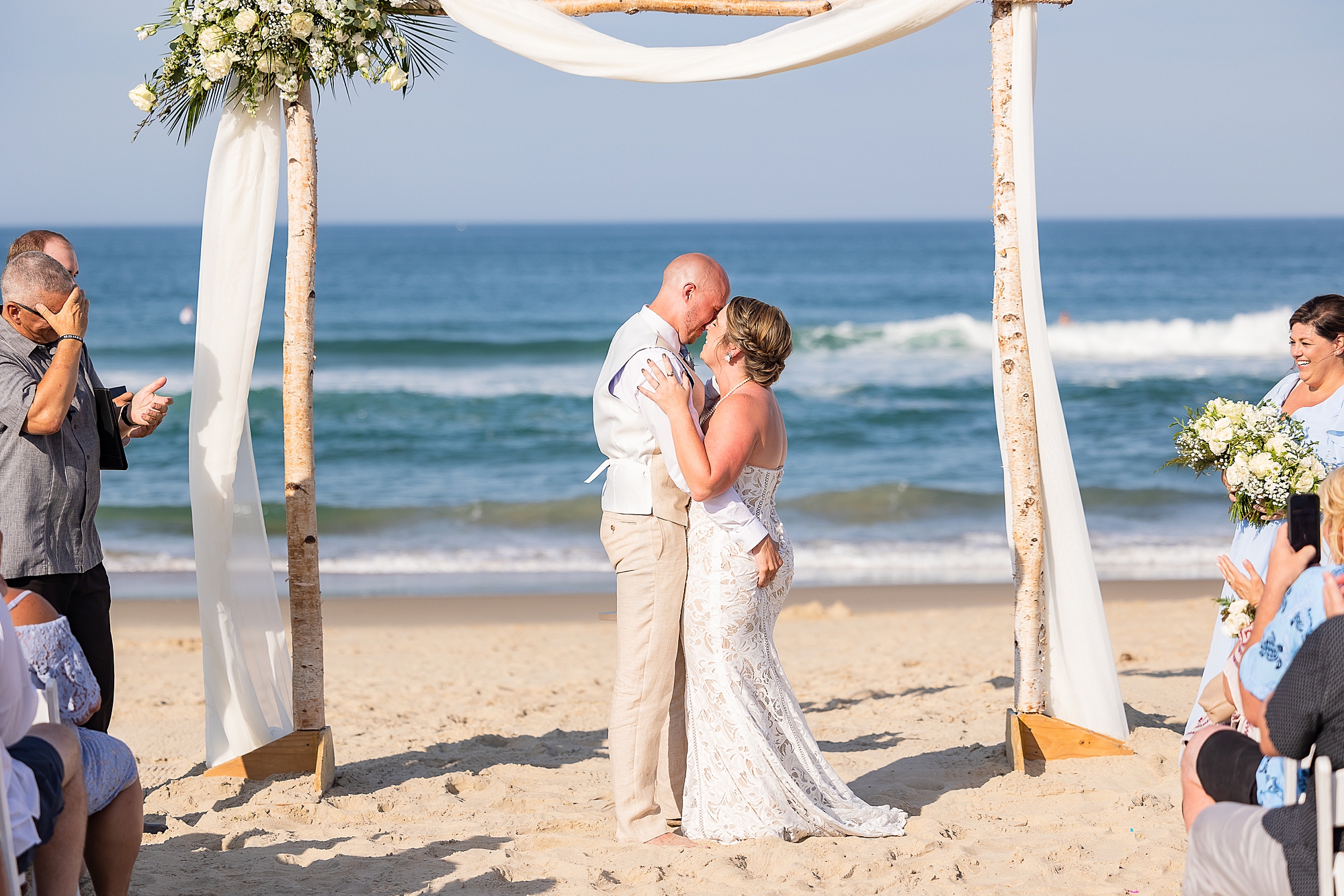 newlyweds kiss under arbor on beach