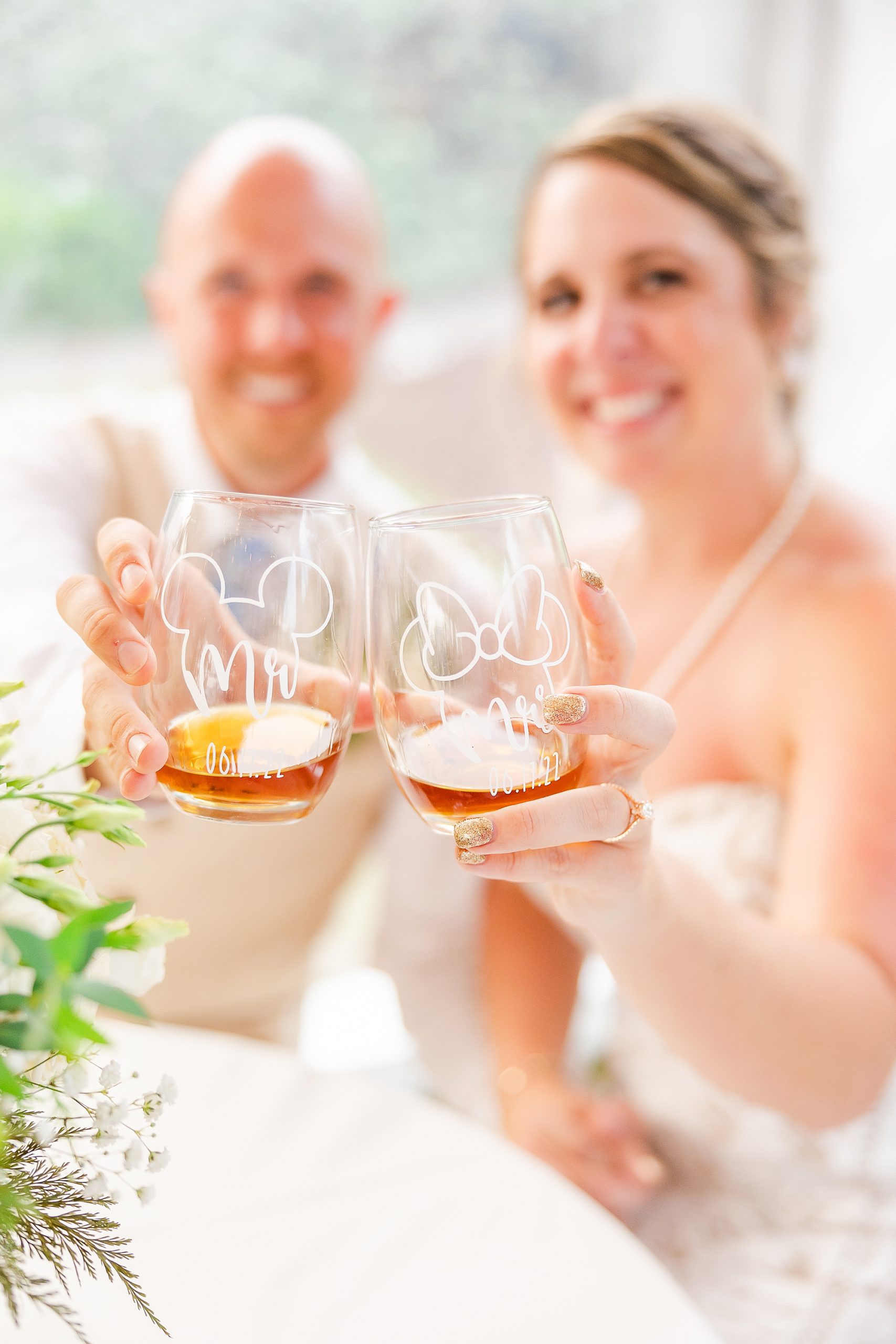 couple holds up glasses of whiskey during wedding day at beach house 
