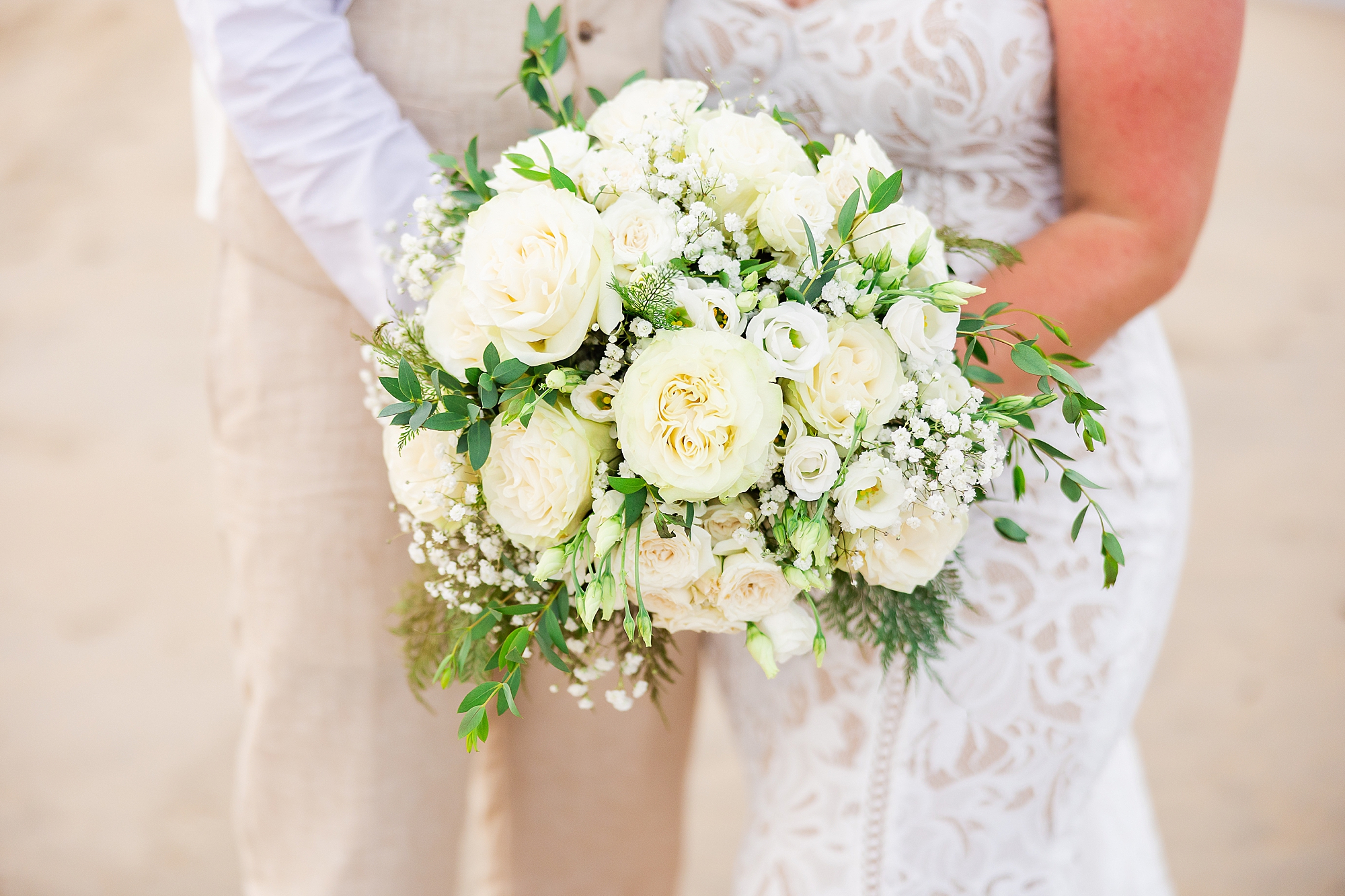 bride and groom hold bouquet of white and yellow flowers. 