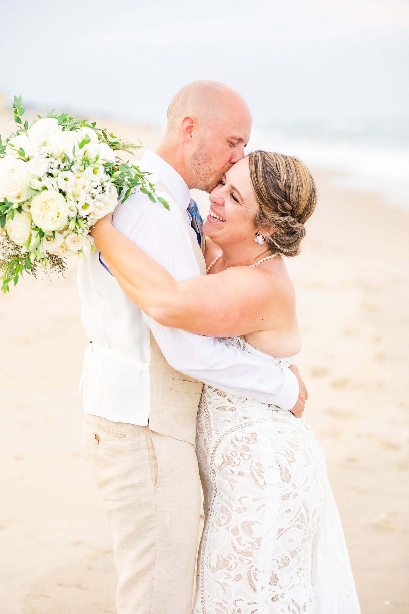 bride laughs hugging groom during beach wedding photos 