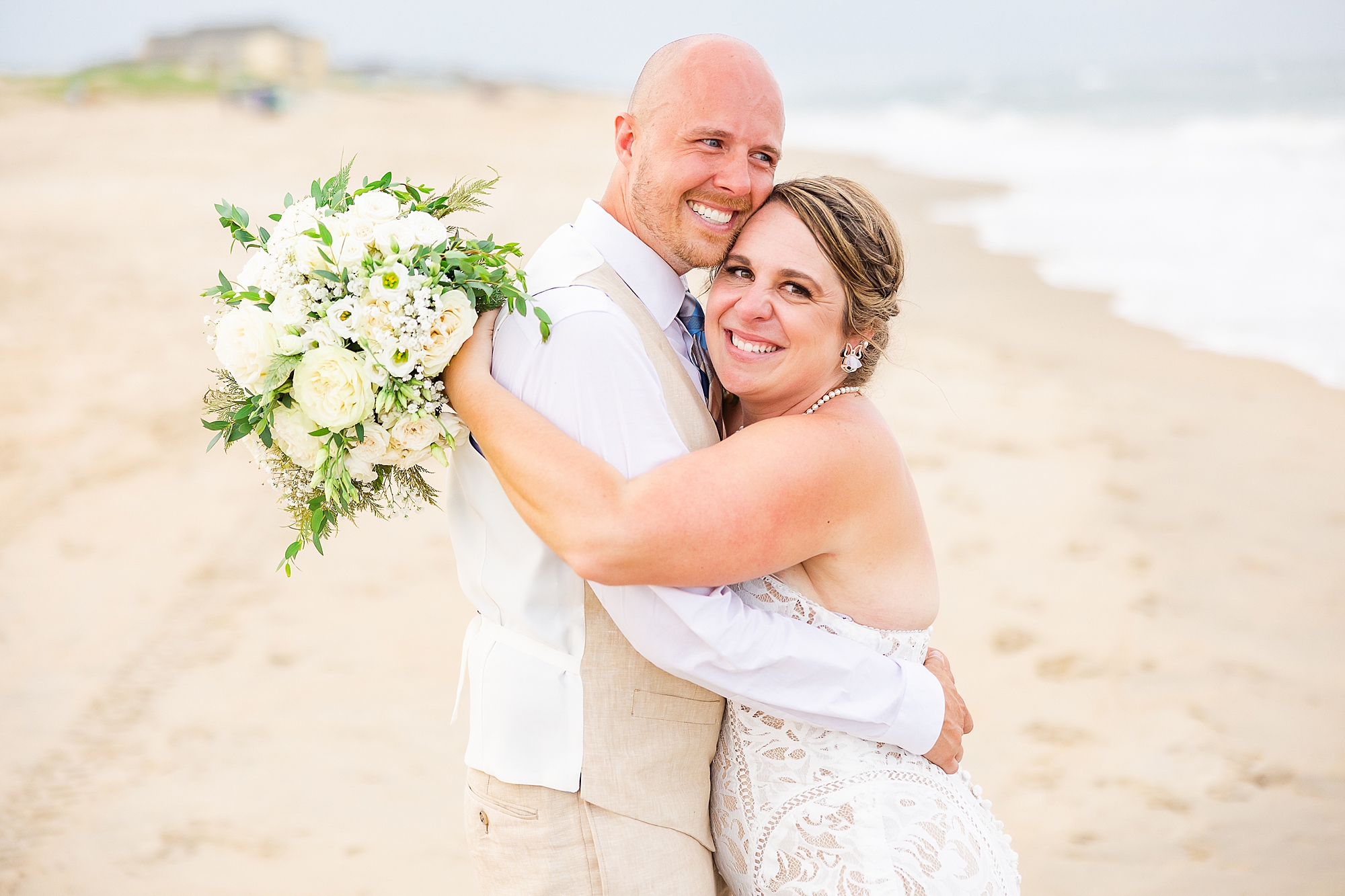 newlyweds hug on beach during portraits at sunset