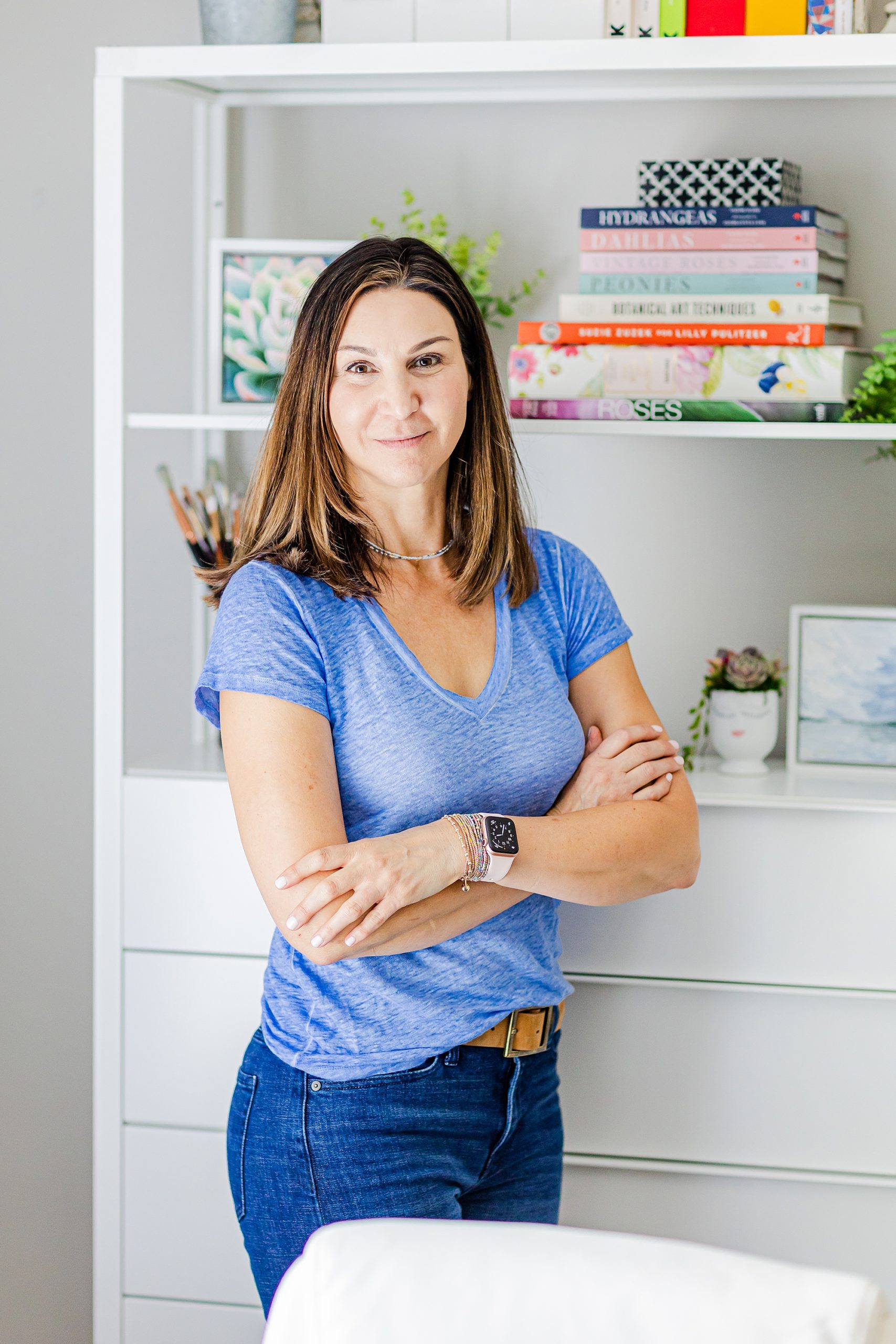 woman stands with arms crossed by bookshelf in Charlotte home studio