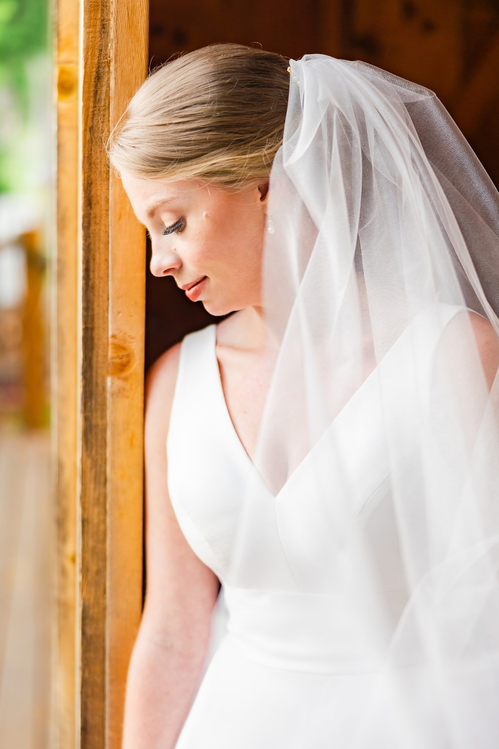 bride leans head against wooden door with veil around shoulders