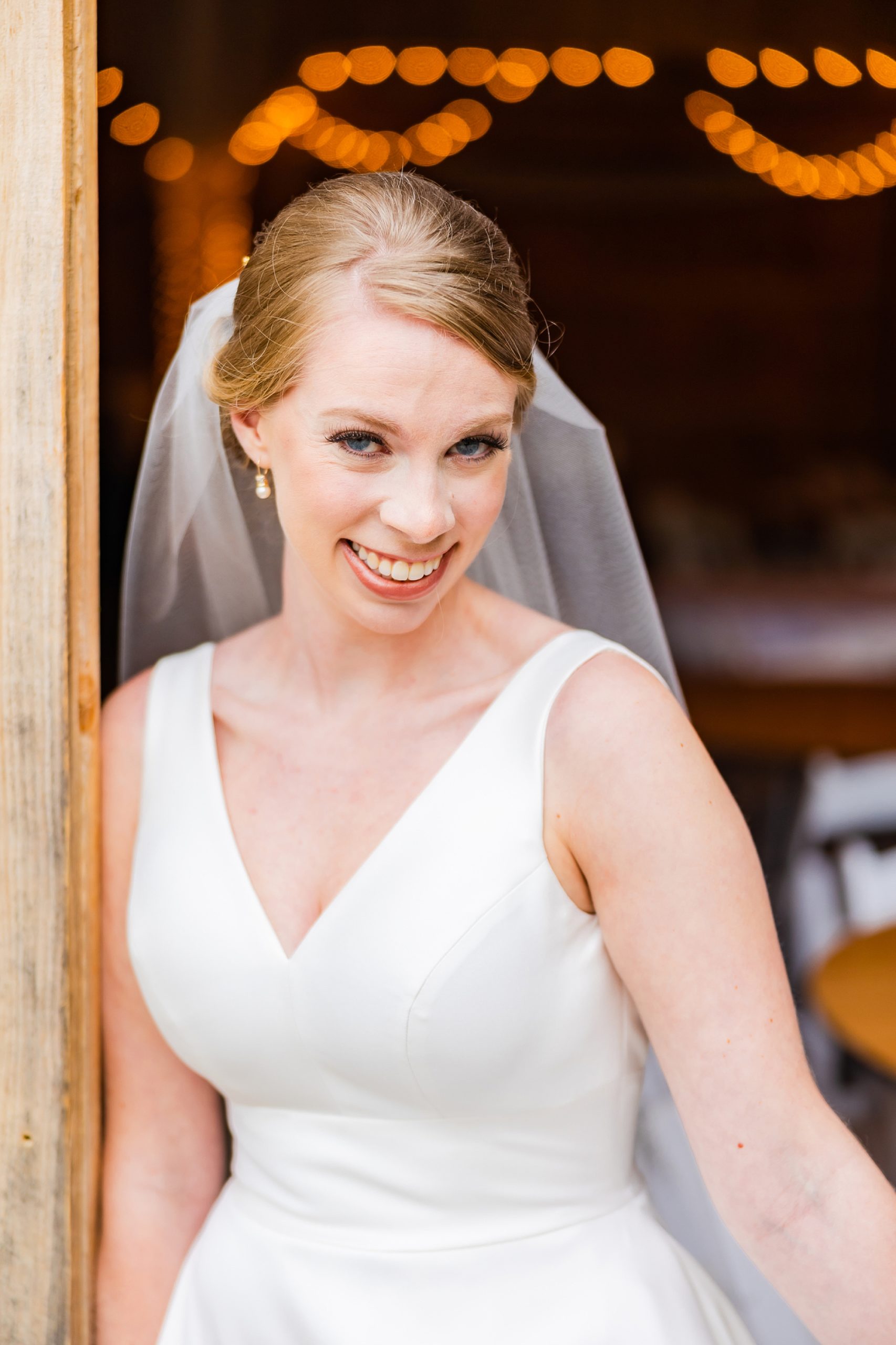 bride smiles standing in doorway of barn in Winston-Salem
