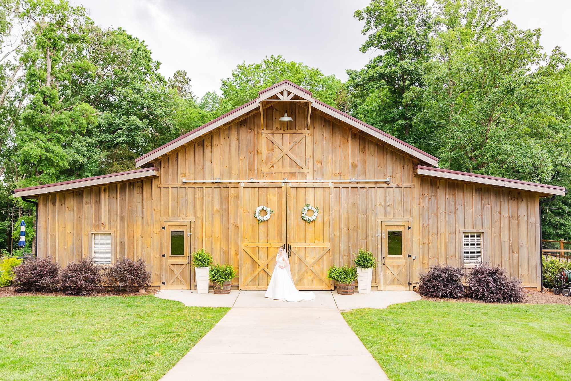 bride stands in wedding gown by wooden barn at Old Homeplace Vineyards