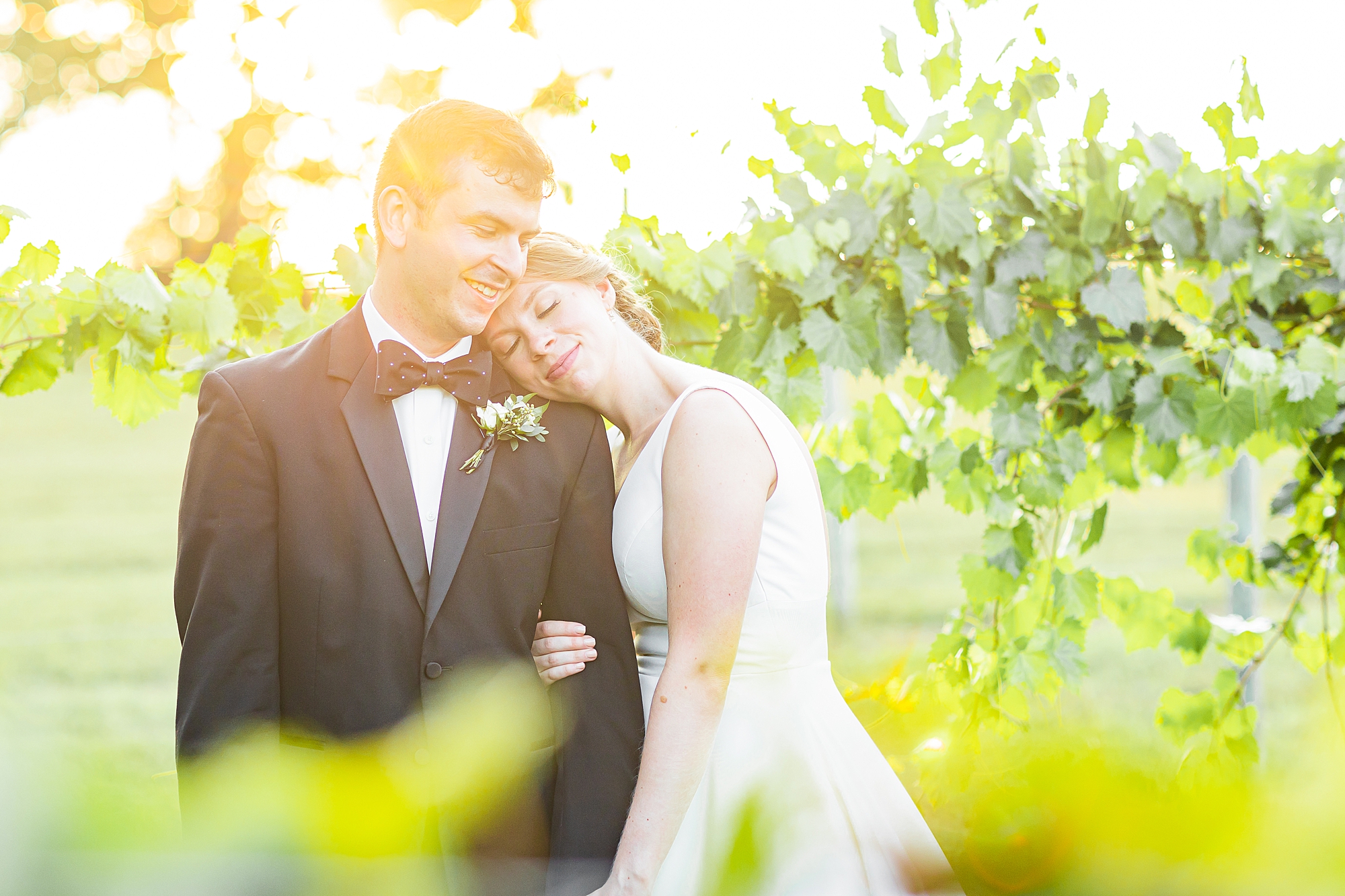 bride leans on groom's shoulder in between vines at Old Homeplace Vineyard