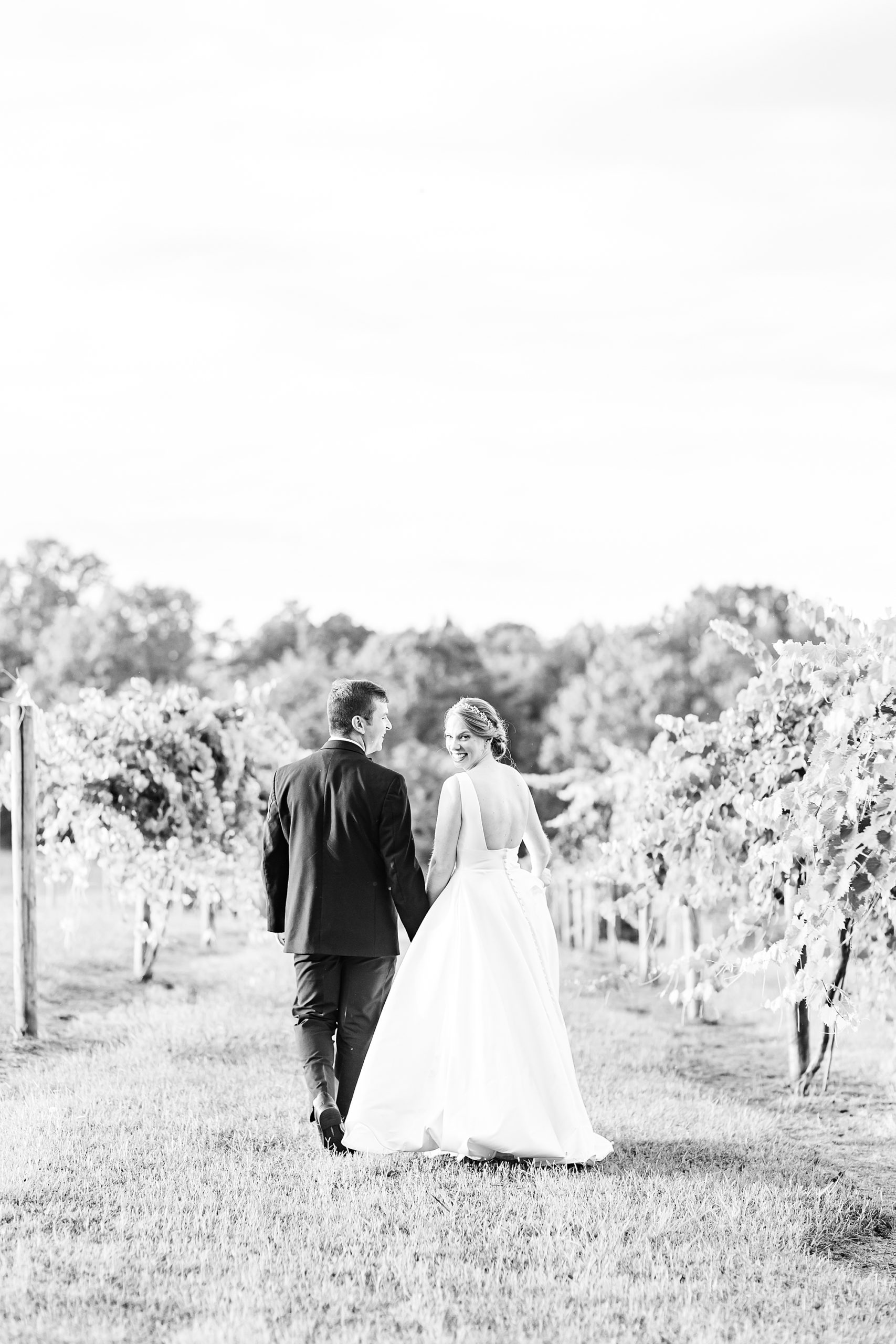 couple holds hands walking through vines at Old Homeplace Vineyard