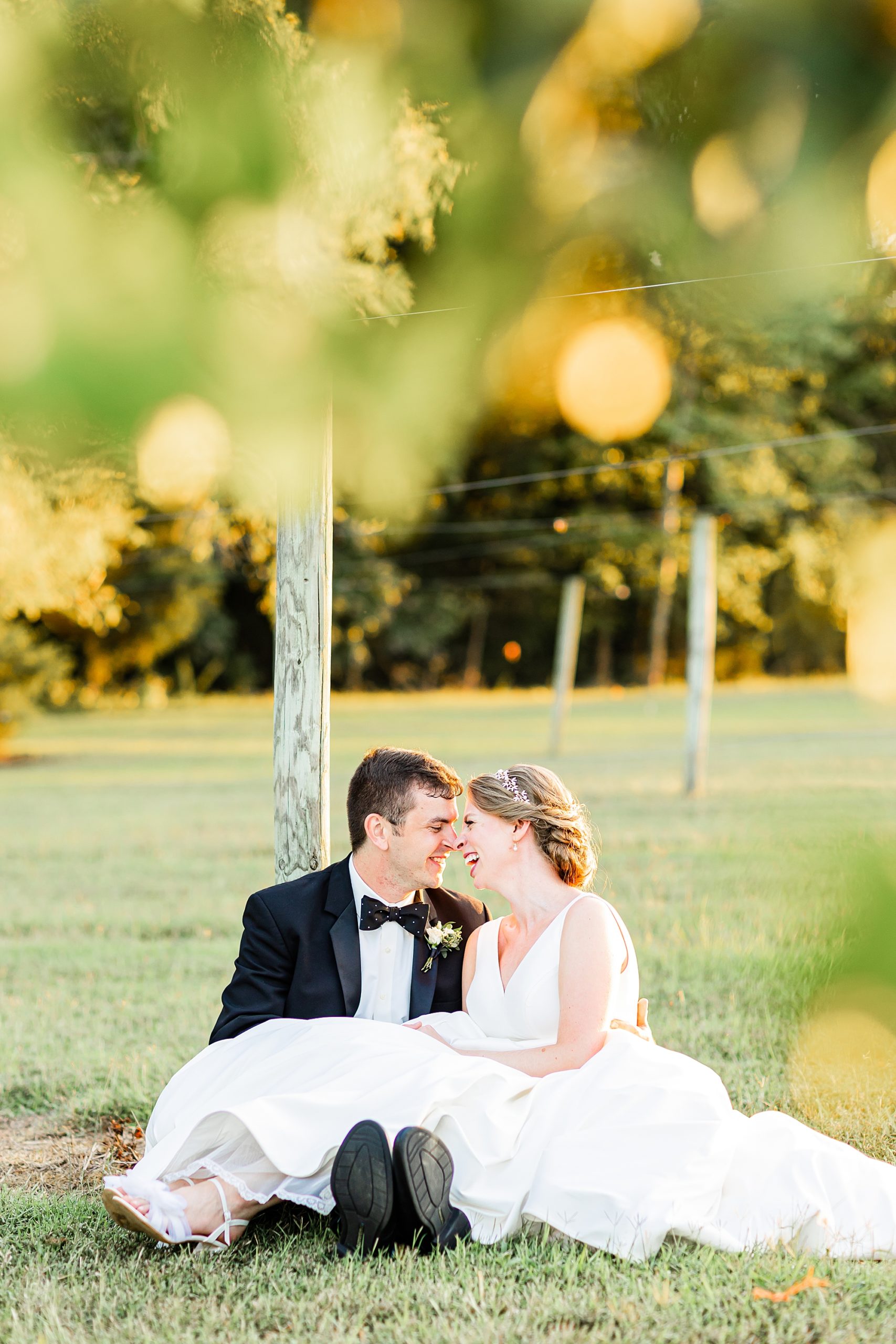 bride and groom sit by wooden pole in vineyard
