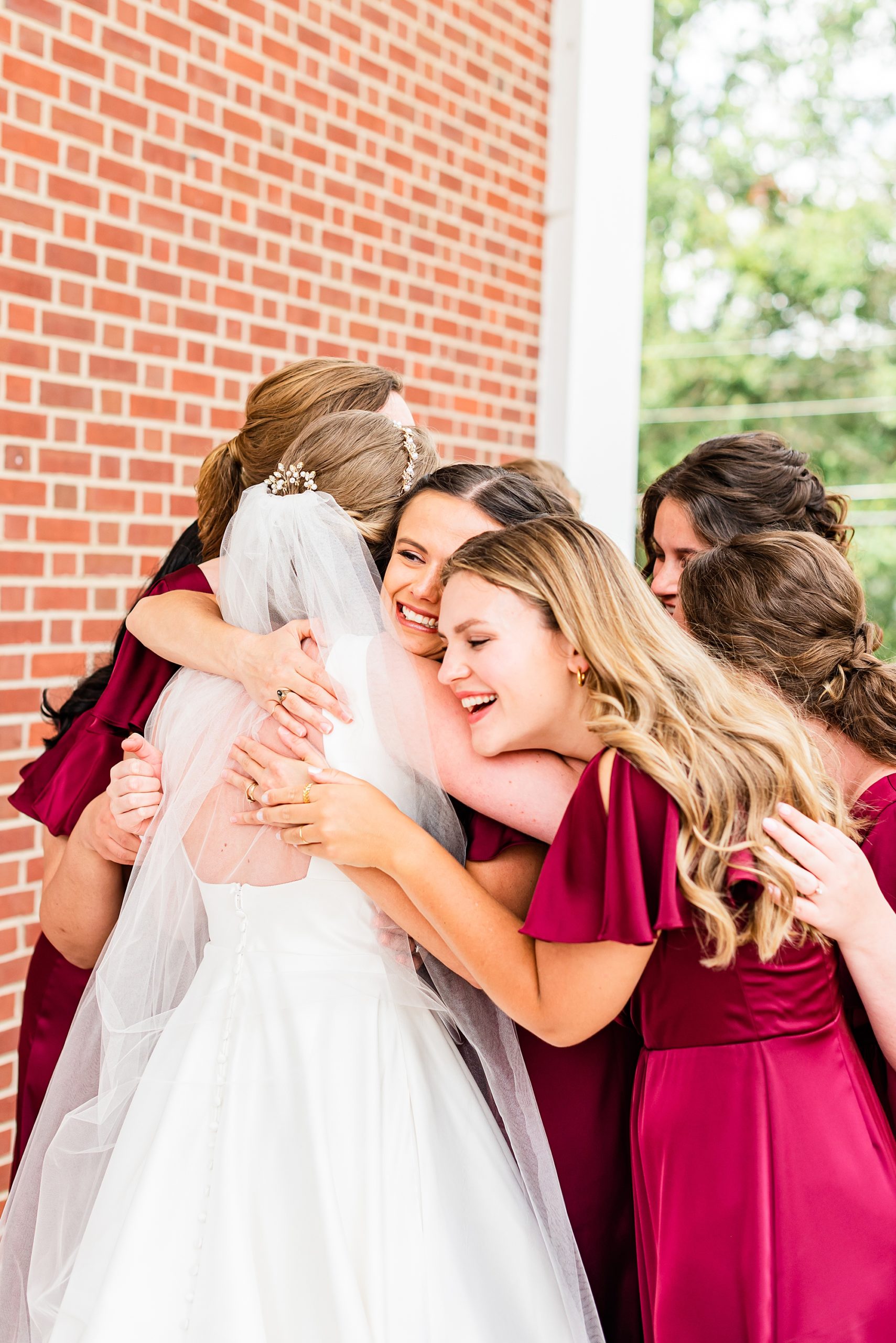 bridesmaids in red gowns hug bride outside church 