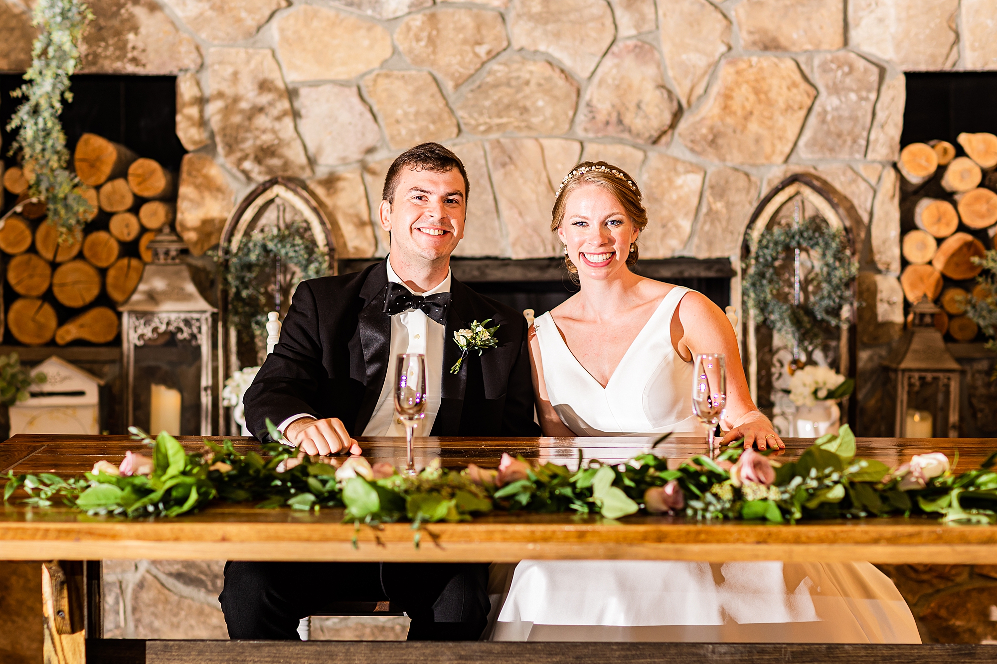 newlyweds sit at sweetheart table by stone fireplace at Old Homeplace Vineyard
