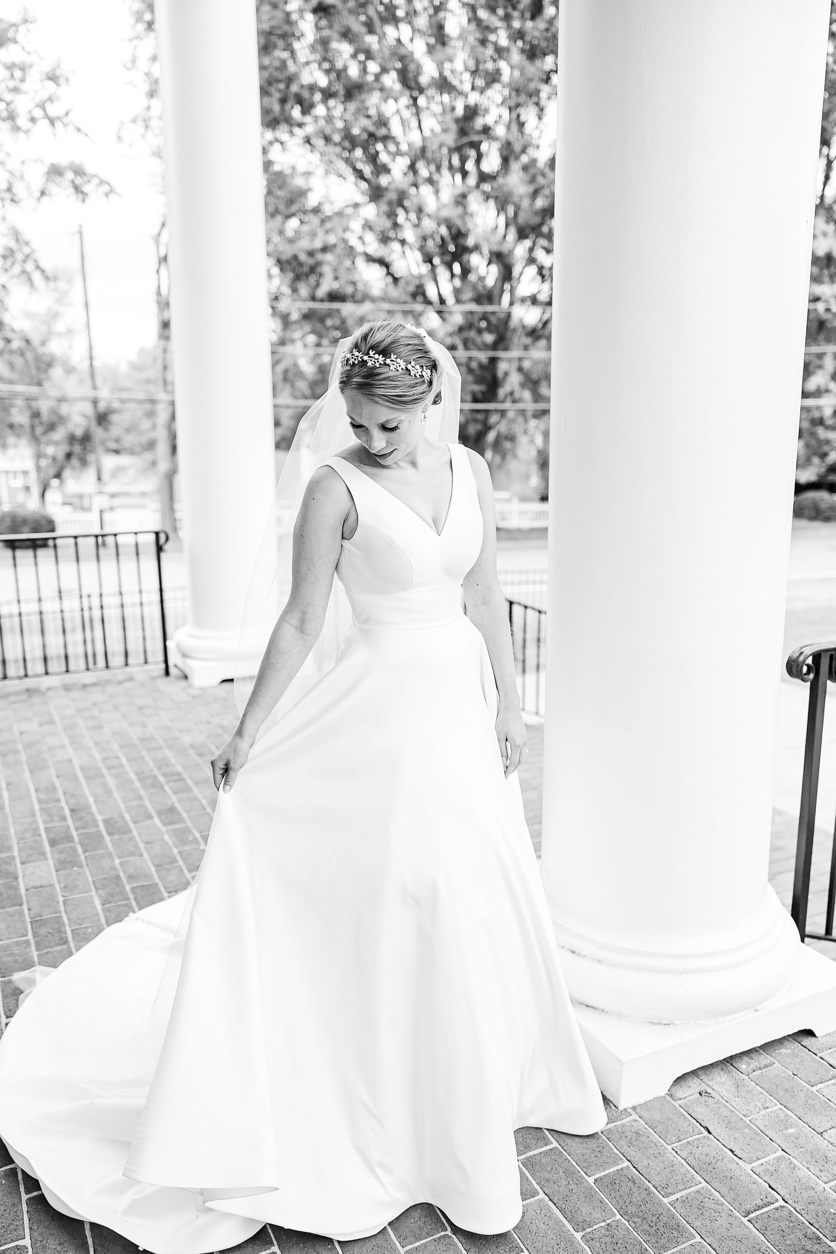 bride looks down at skirt of wedding gown on porch of College Park Baptist Church