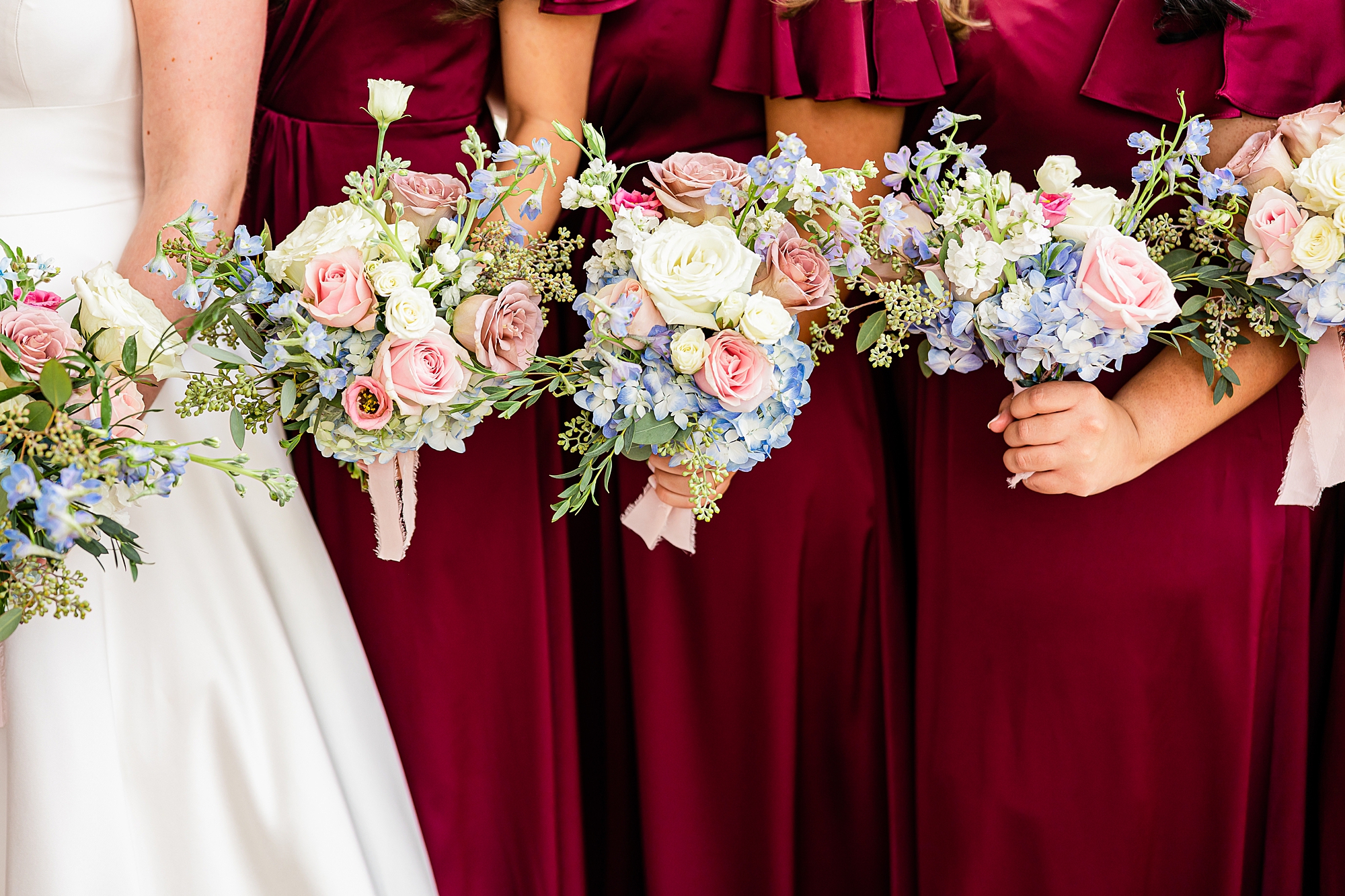 bridesmaids hold bouquets of pastel flowers wearing burgundy gowns