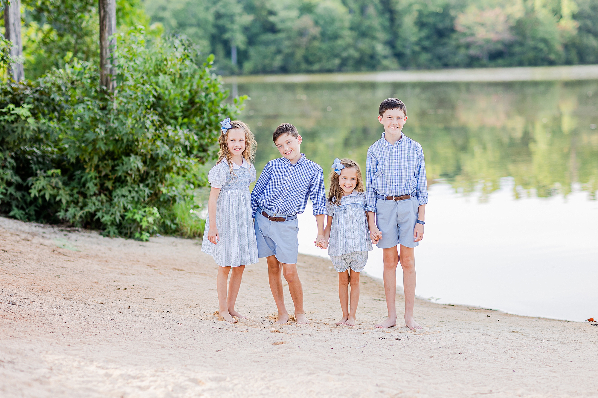 siblings in light blue outfits hug on sand during lakefront family portraits in Charlotte 
