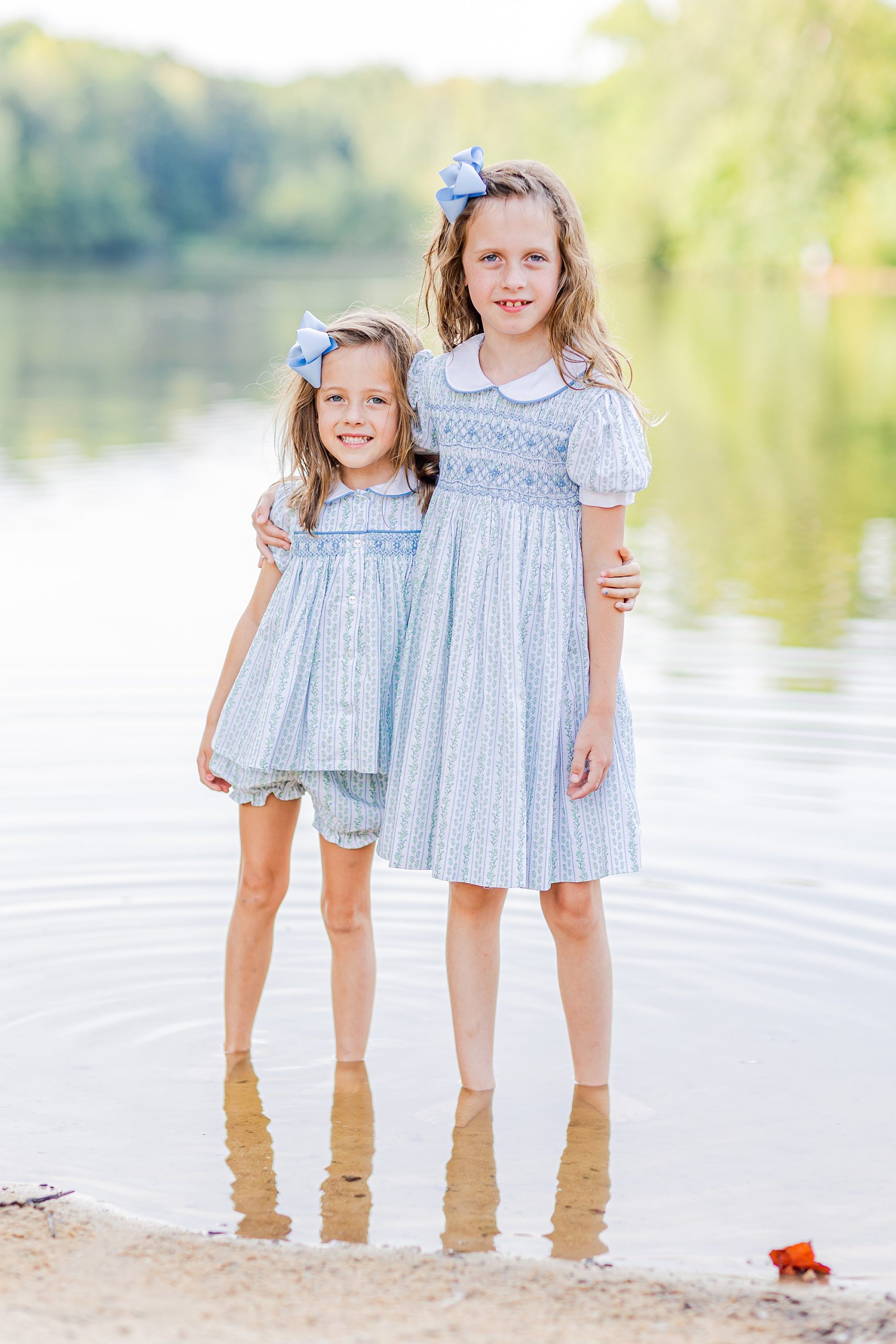 sisters in matching blue dresses and bows hug in Lake Norma