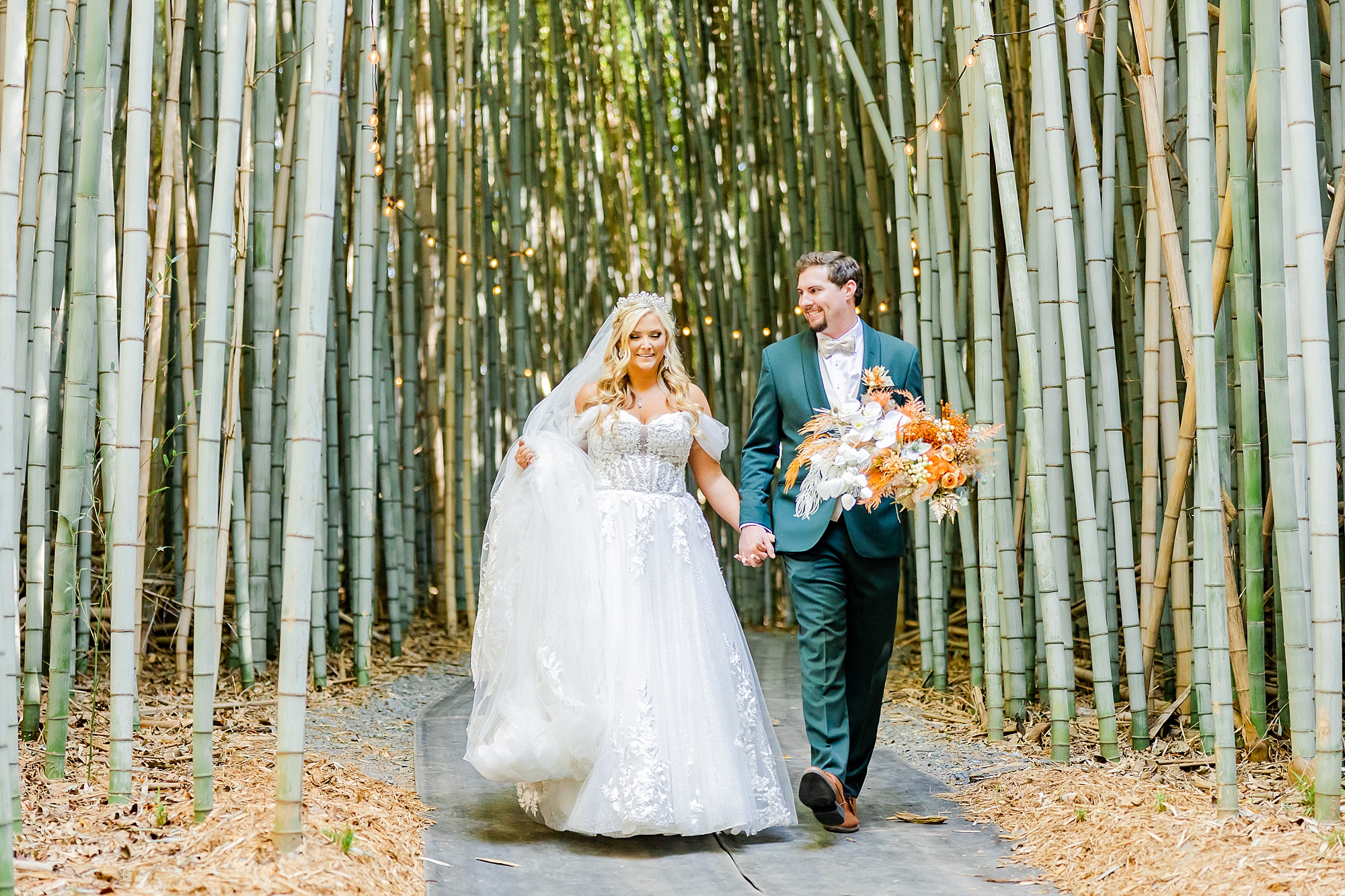 couple walks through bamboo with groom holding ride's bouquet 