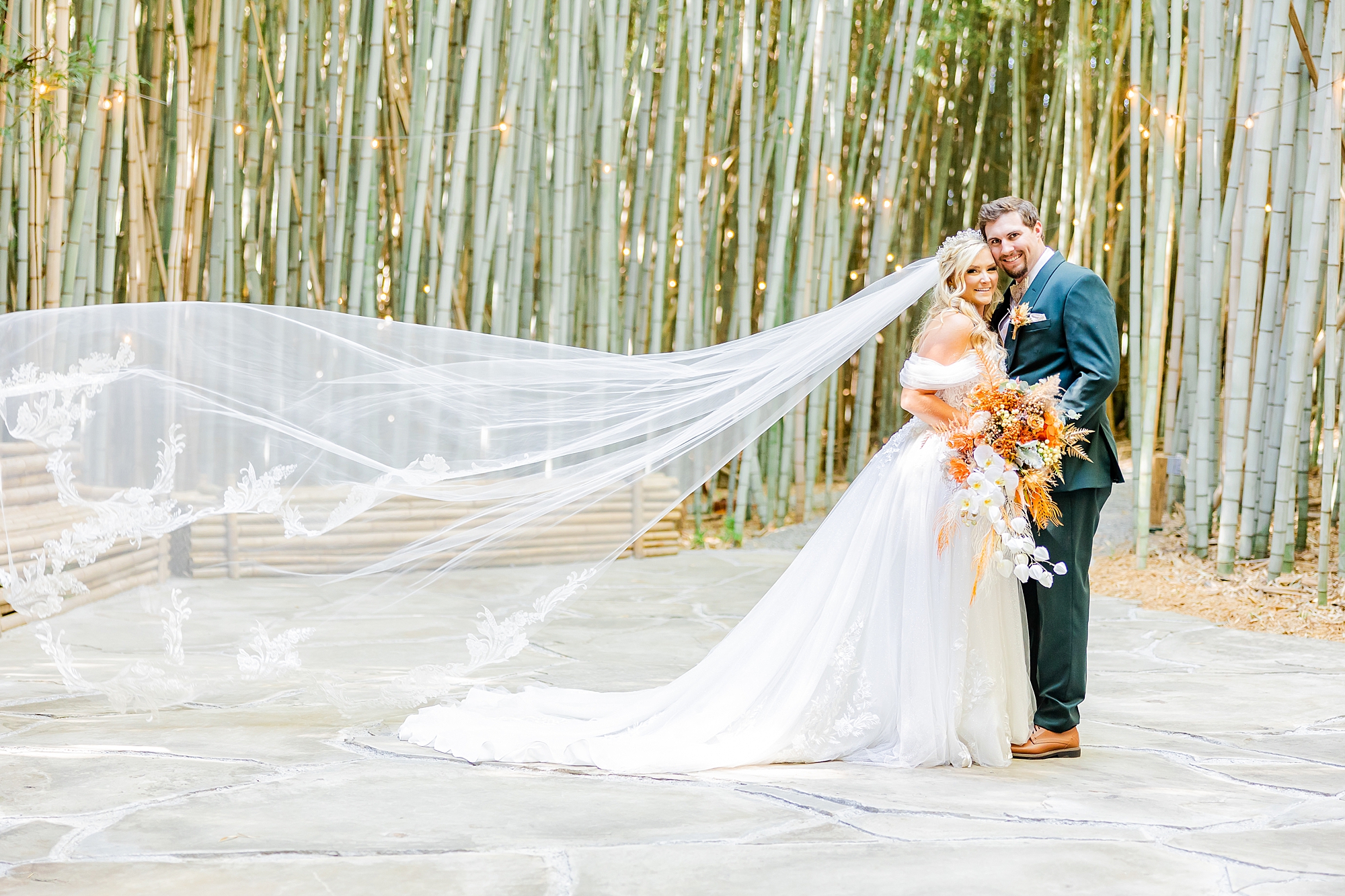 bride and groom hug with bride's veil floating behind them among bamboo shoots 