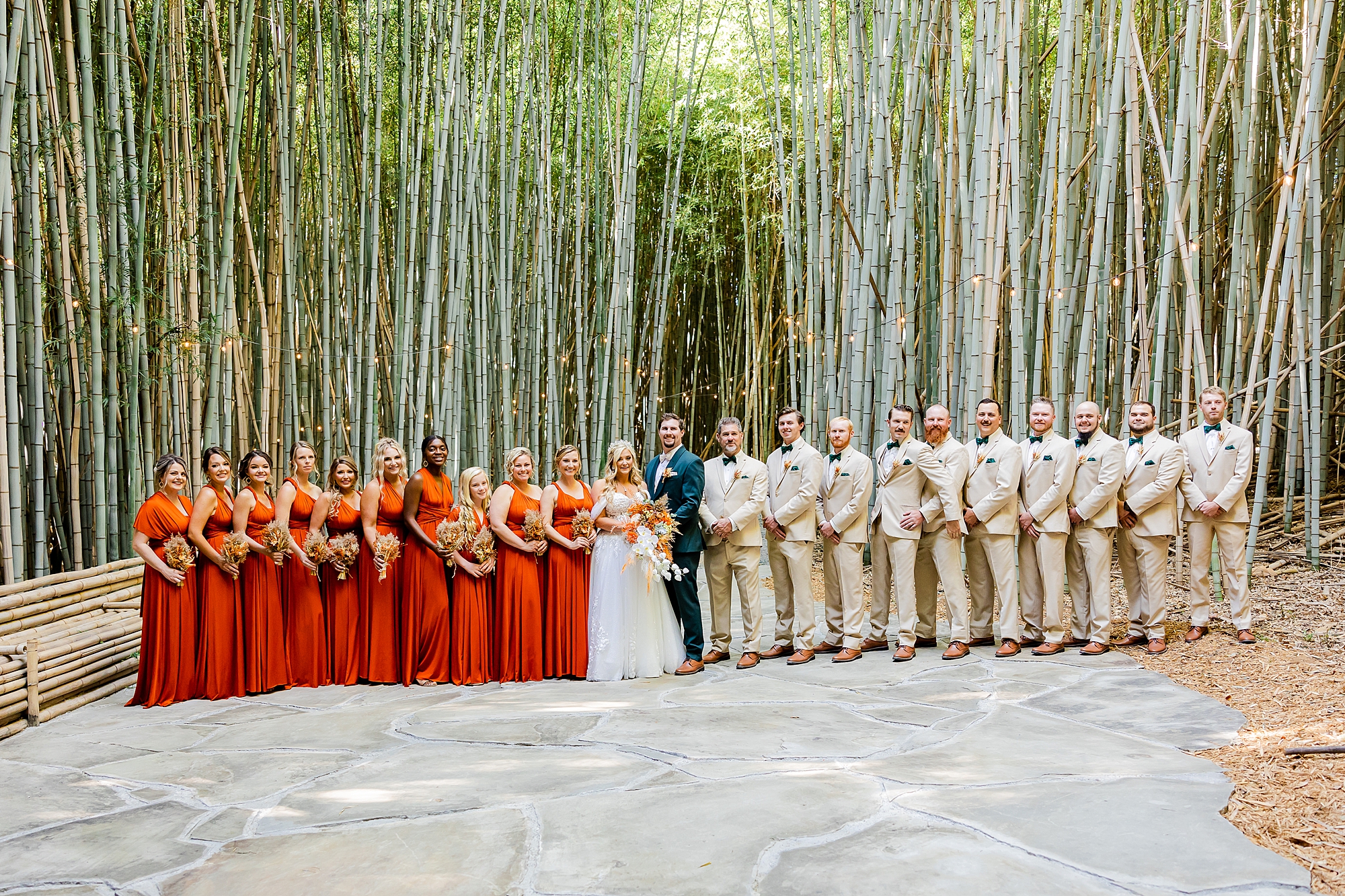 newlyweds pose with wedding party in tan and burnt orange in bamboo forest at Camelot Meadows
