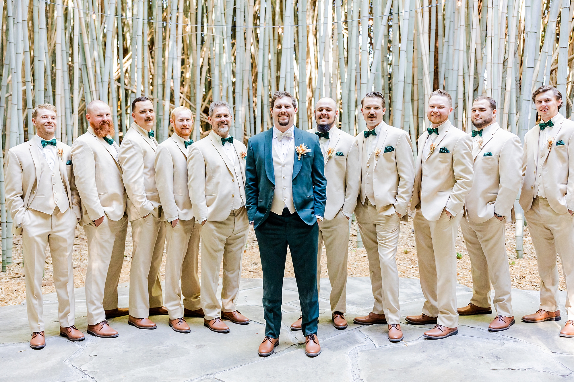 groom stands with groomsmen in tan suits at Camelot Meadows