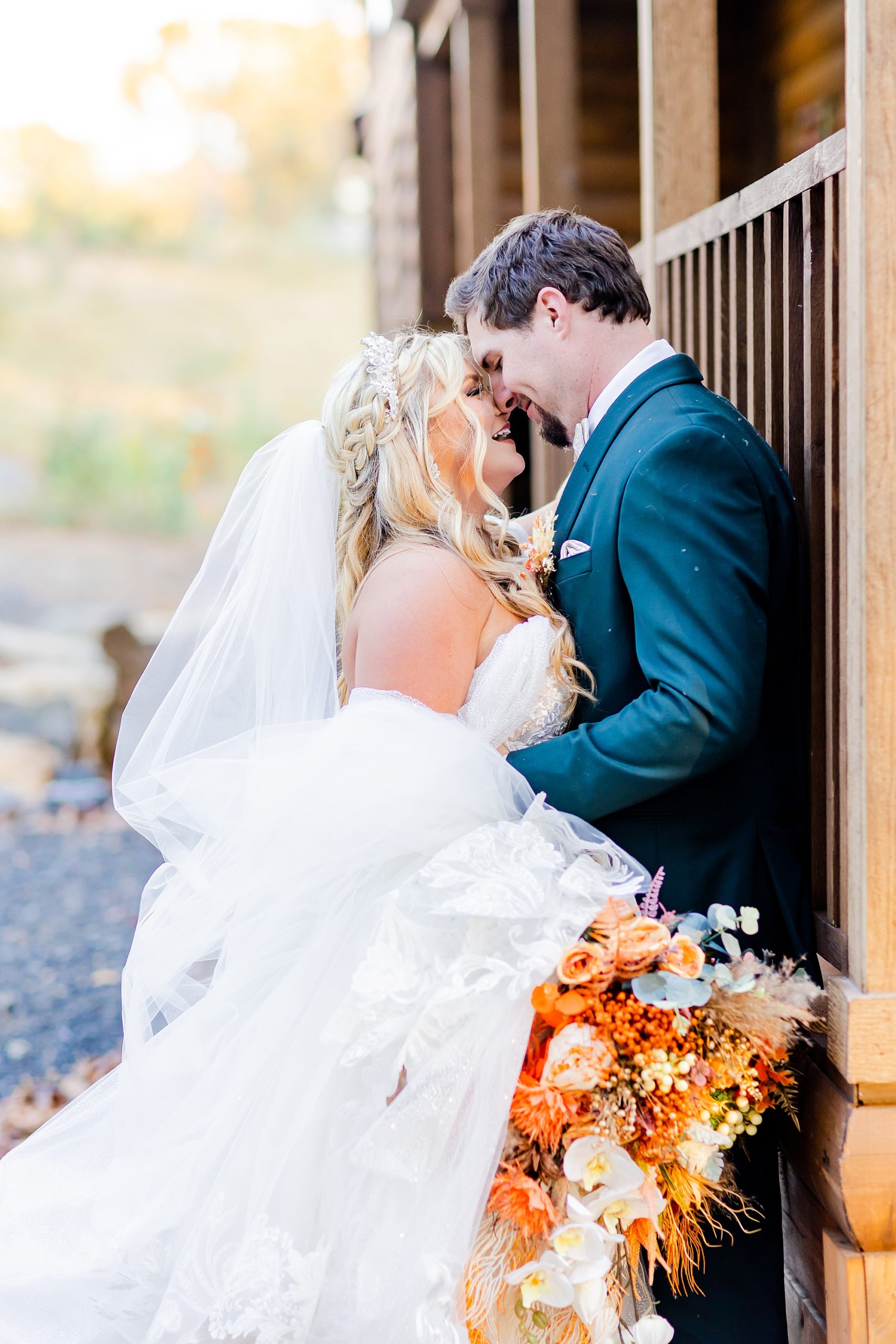 newlyweds laugh with noses touching against wooden cabin at Camelot Meadows