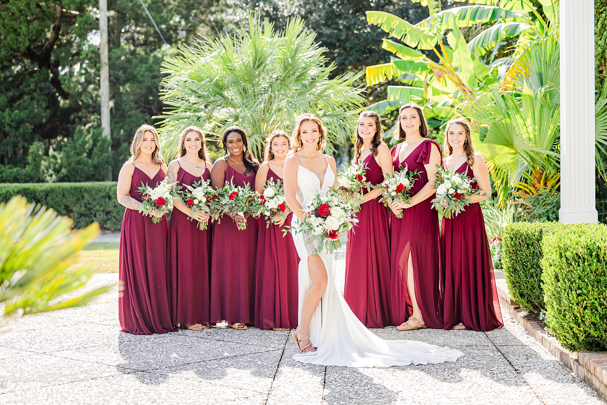 bride and bridesmaids stand outside the Island House with burgundy flowers 