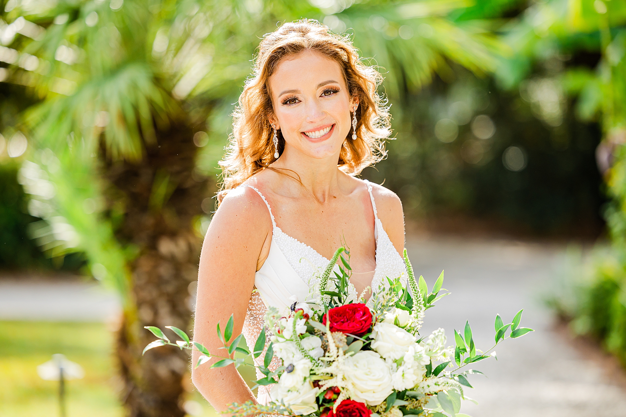 bride smiles in wedding gown holding red and white bouquet in Charleston SC