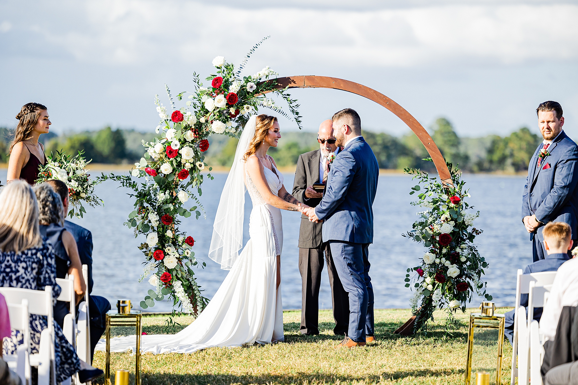 bride and groom exchange vows under wooden arbor with red and white flowers 