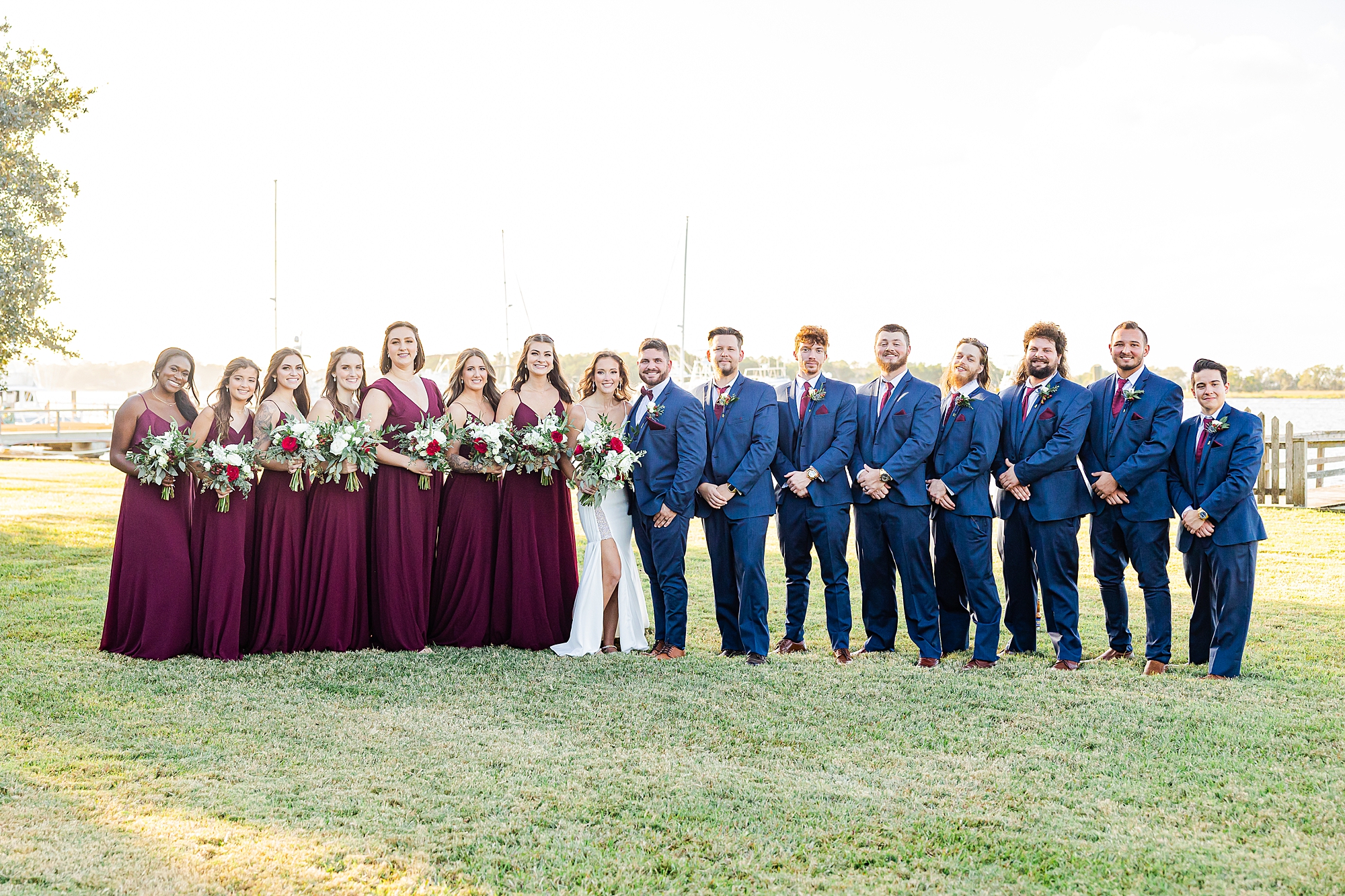 bride and groom stand with wedding party in navy and burgundy during Charleston wedding photos