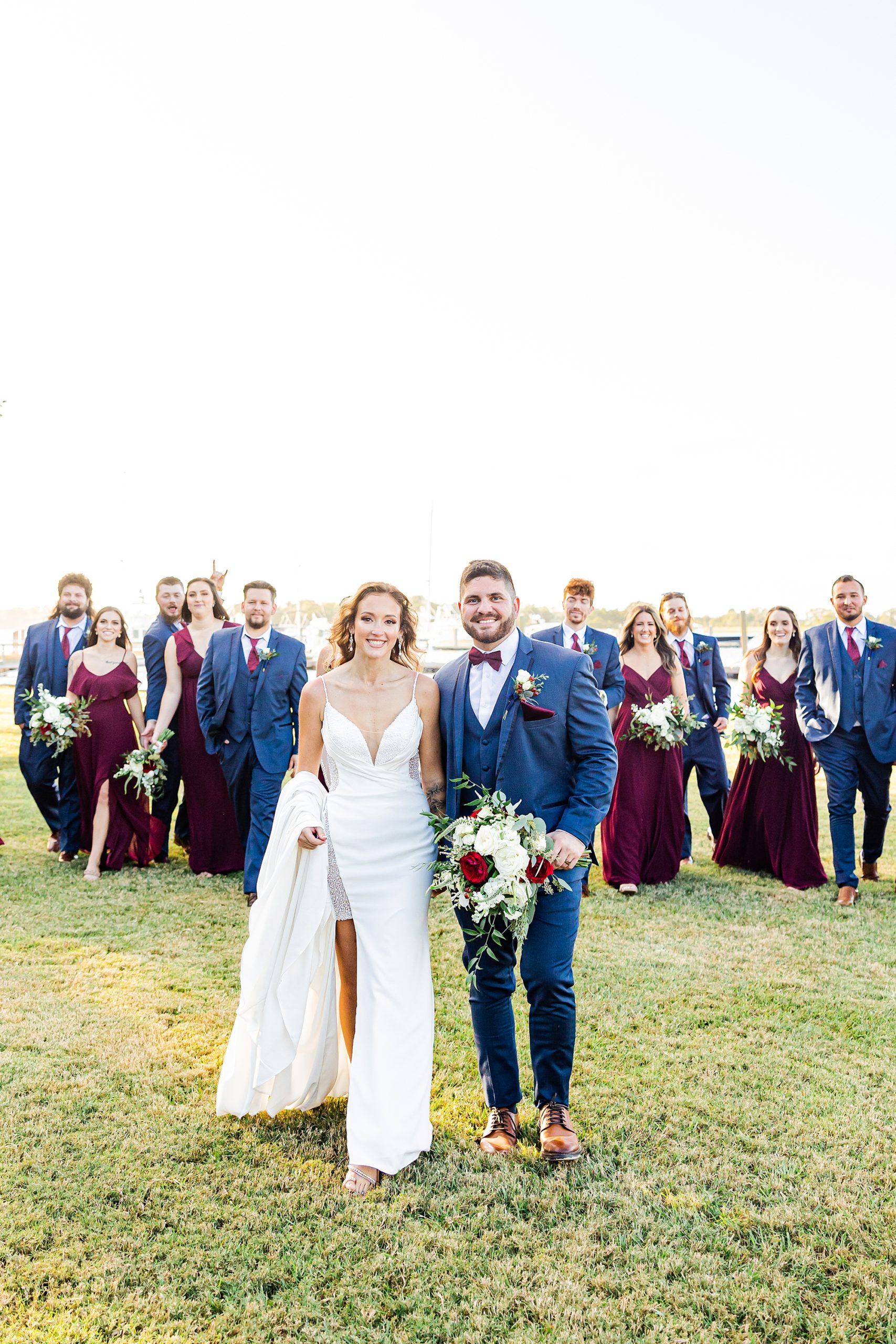 bride and groom walk with wedding party in navy and burgundy 