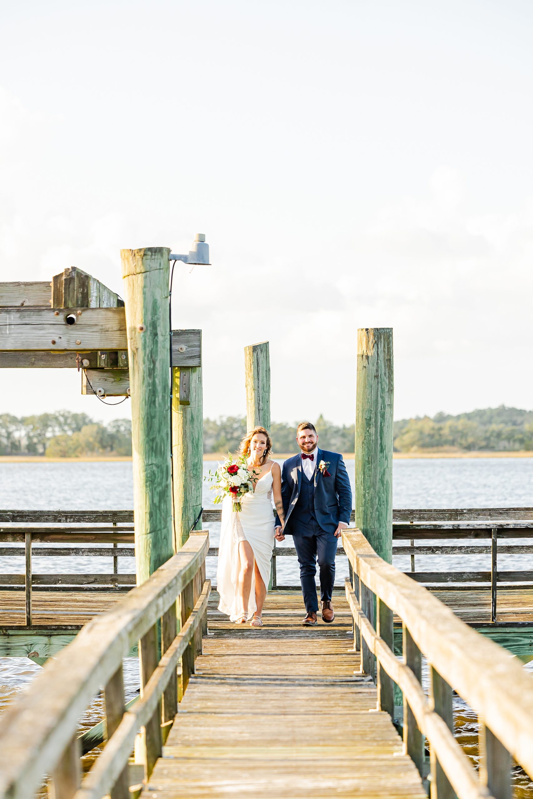 bride and groom walk up wooden pier during John's Island wedding portraits 