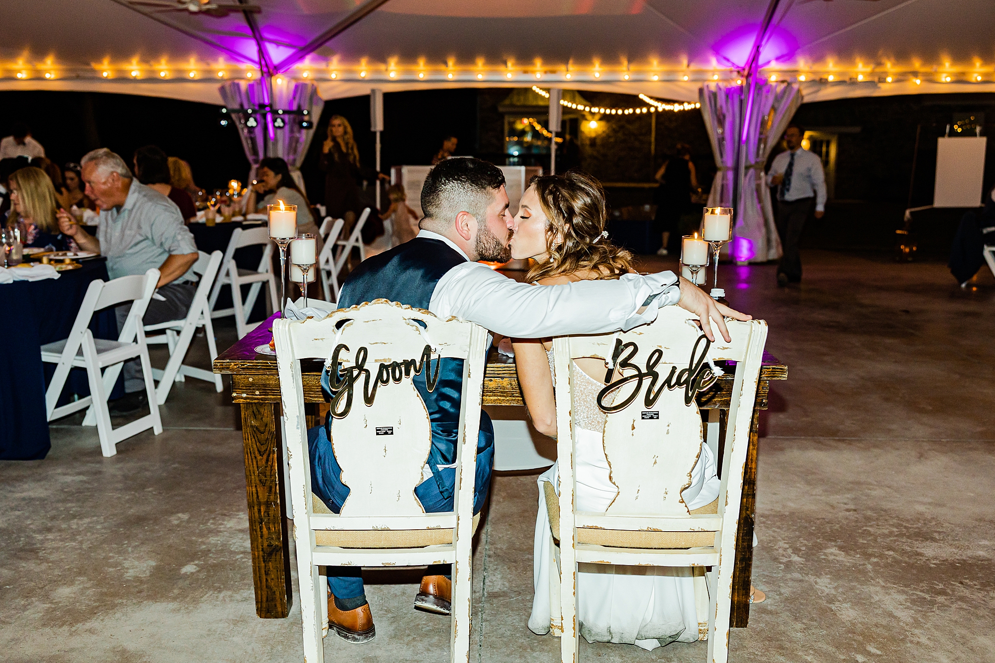 bride and groom kiss sitting in Bride and Groom chairs 