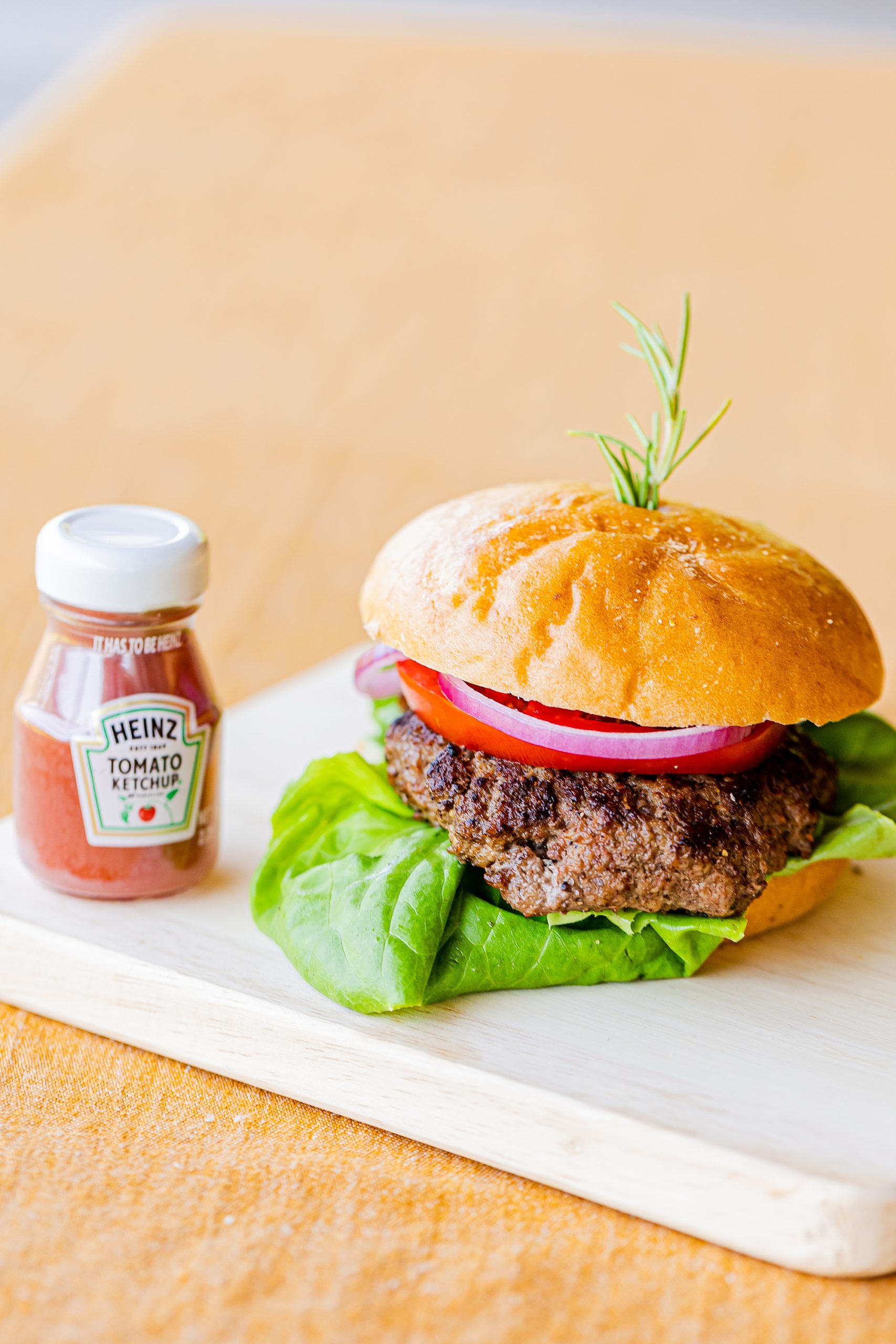 burger with onion, tomato, and lettuce sits by little bottle of ketchup 
