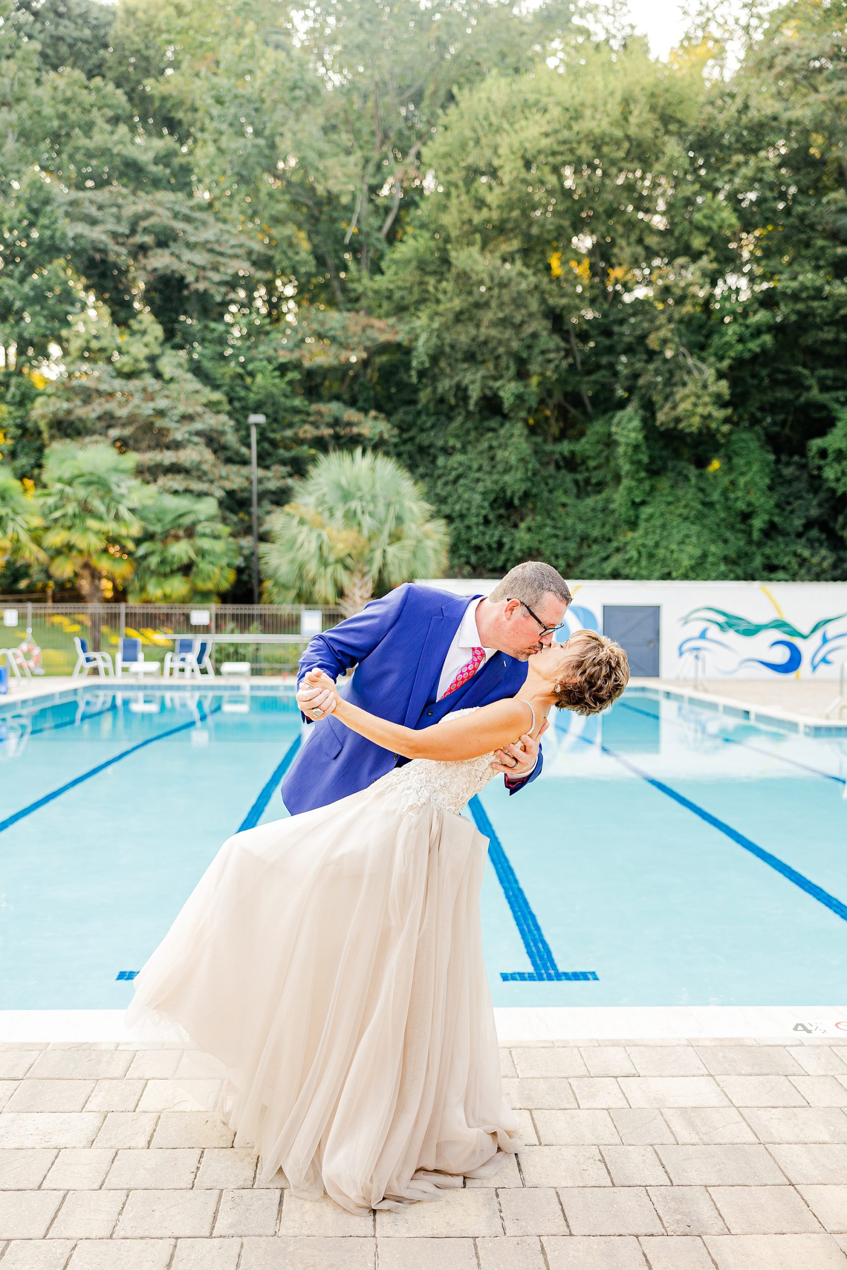 groom in bright blue suit dips bride kissing her by pool