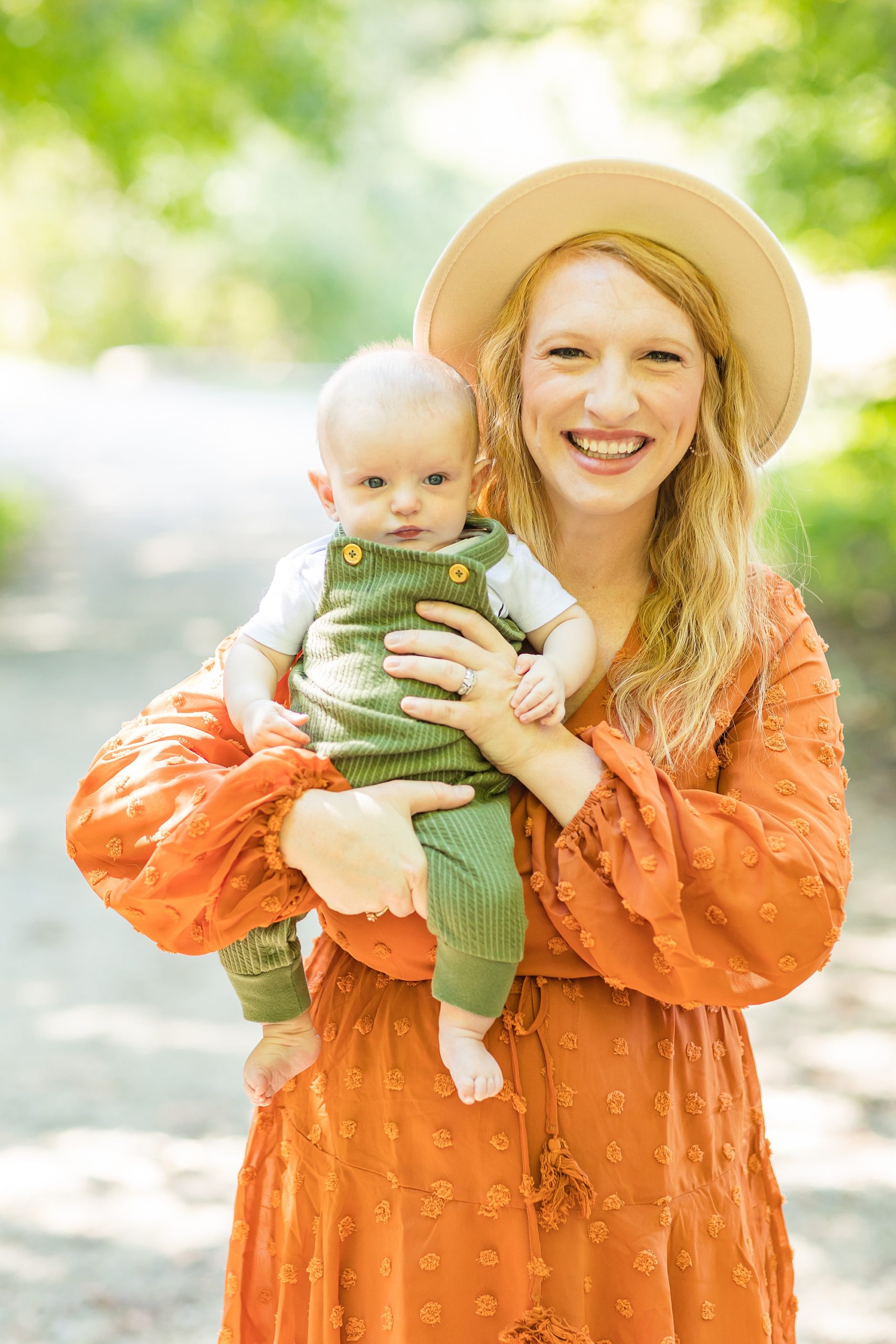 mom in orange dress poses with 6 month old baby in overalls
