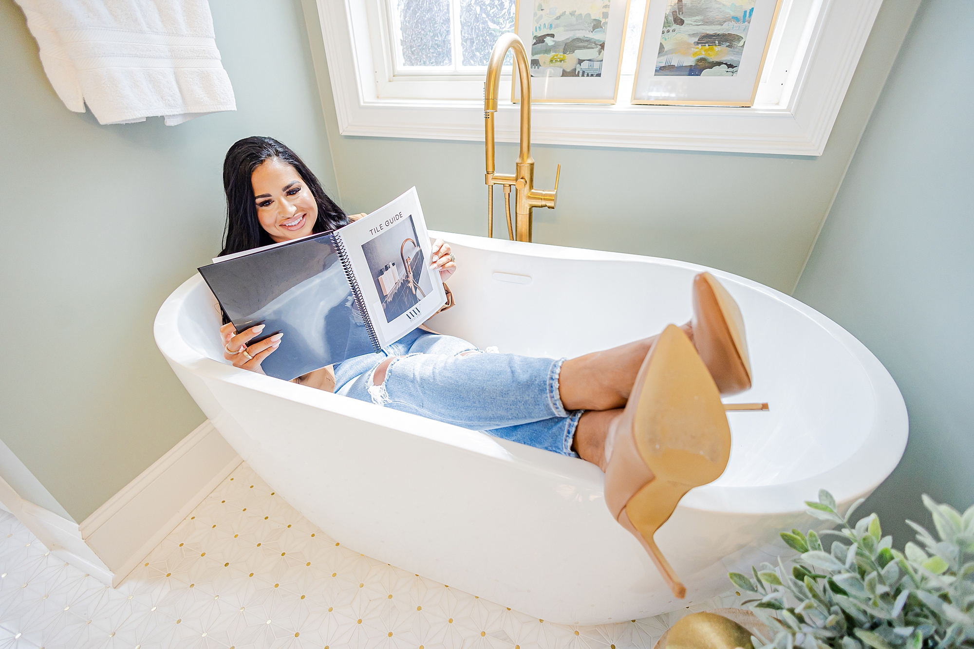 interior designer sits in bathtub with feet on edge of tub looking at magazine 