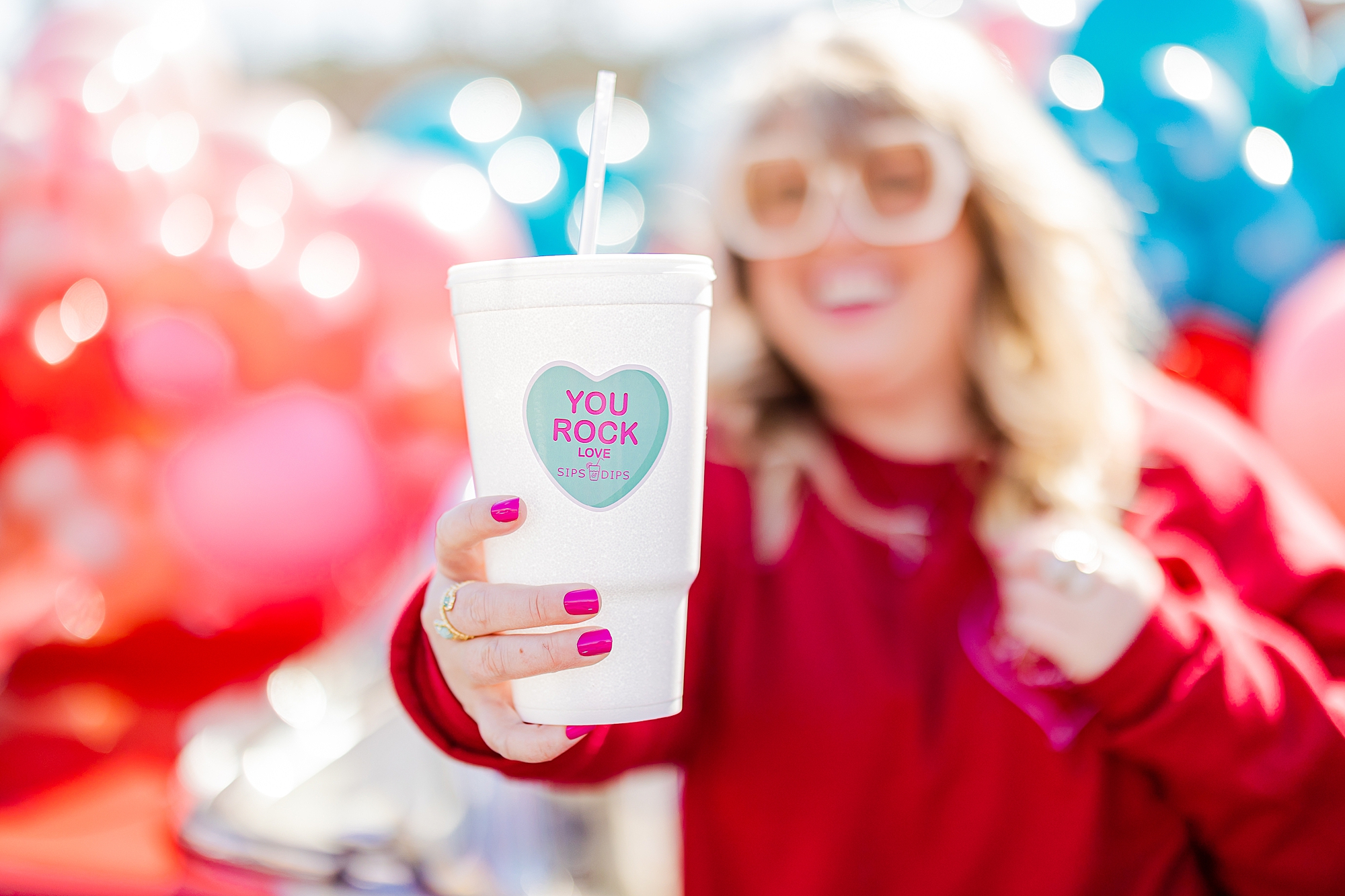 woman holds out soda cup with candy heart that says "you rock" 