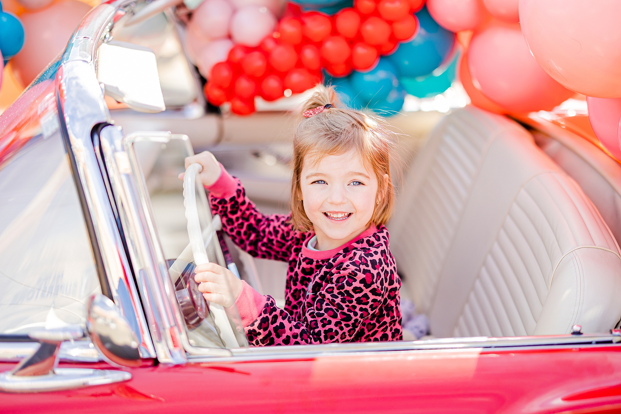 toddler in pink sweater smiles pretending to drive car 