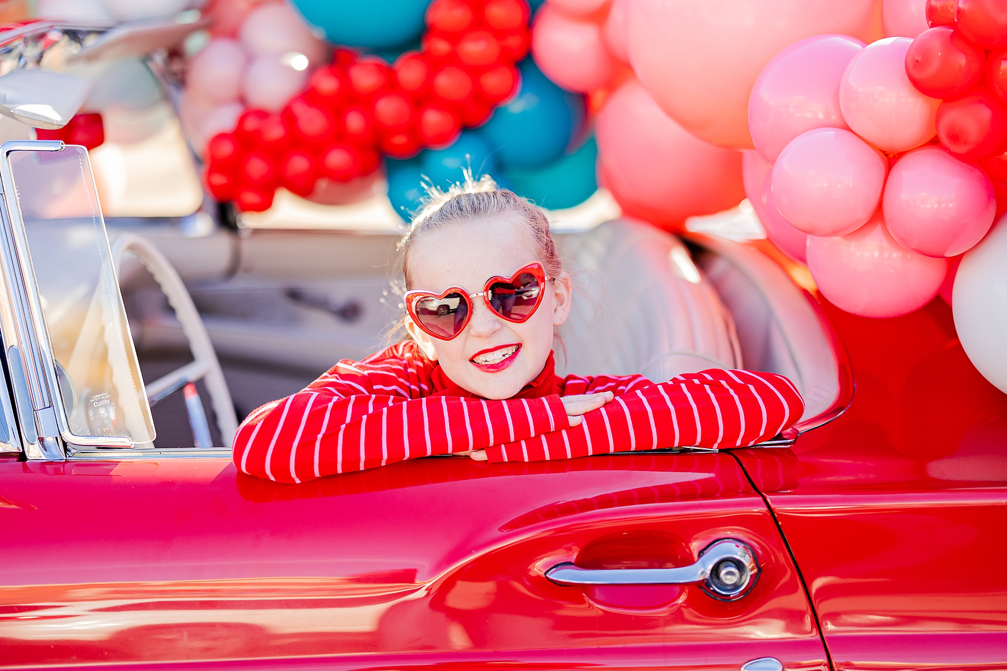 girl in red sweater with heart sunglasses lean on door of red Thunderbird 