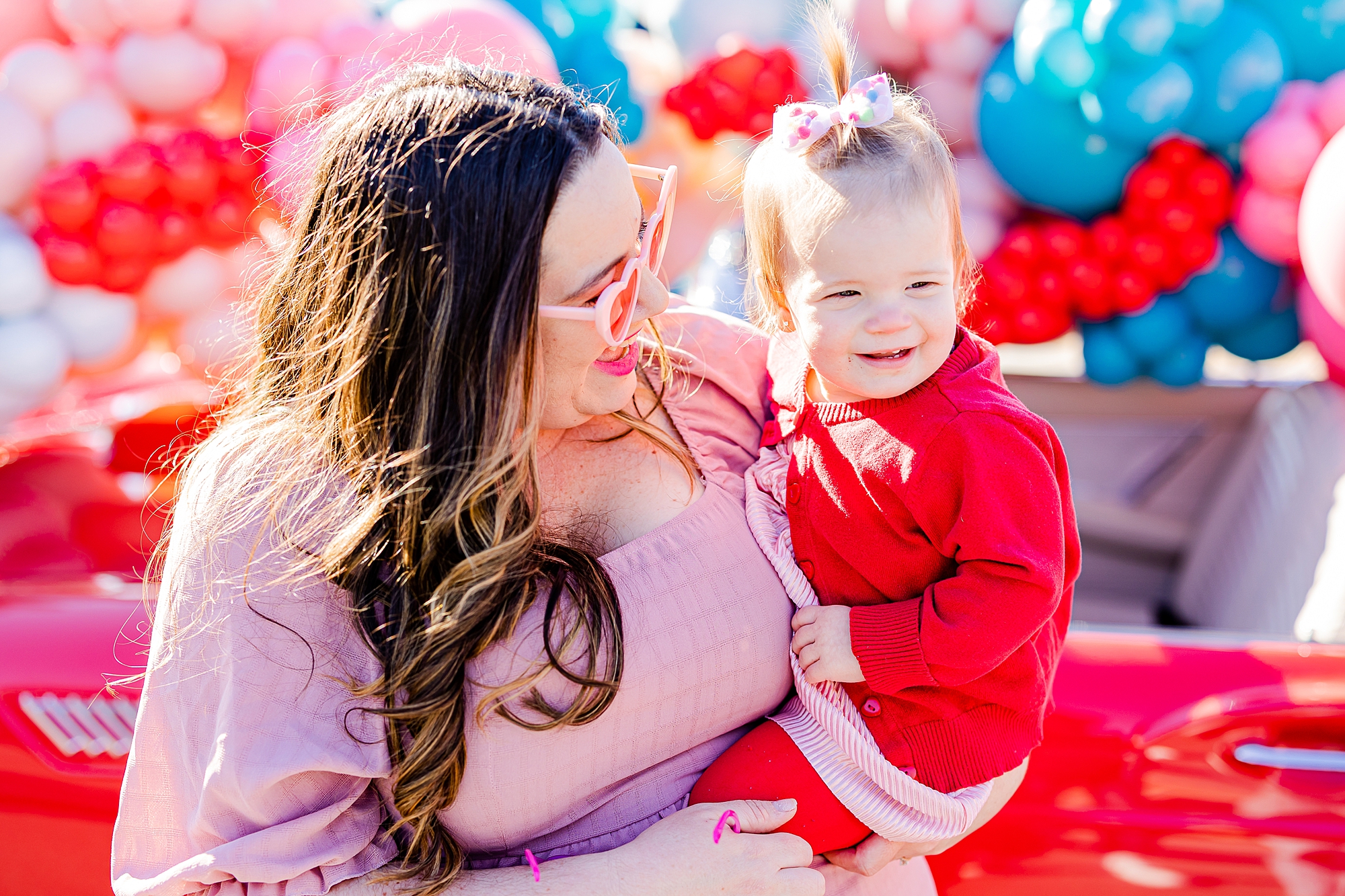 woman in pink dress smiles at daughter in red dress by Red Thunderbird 