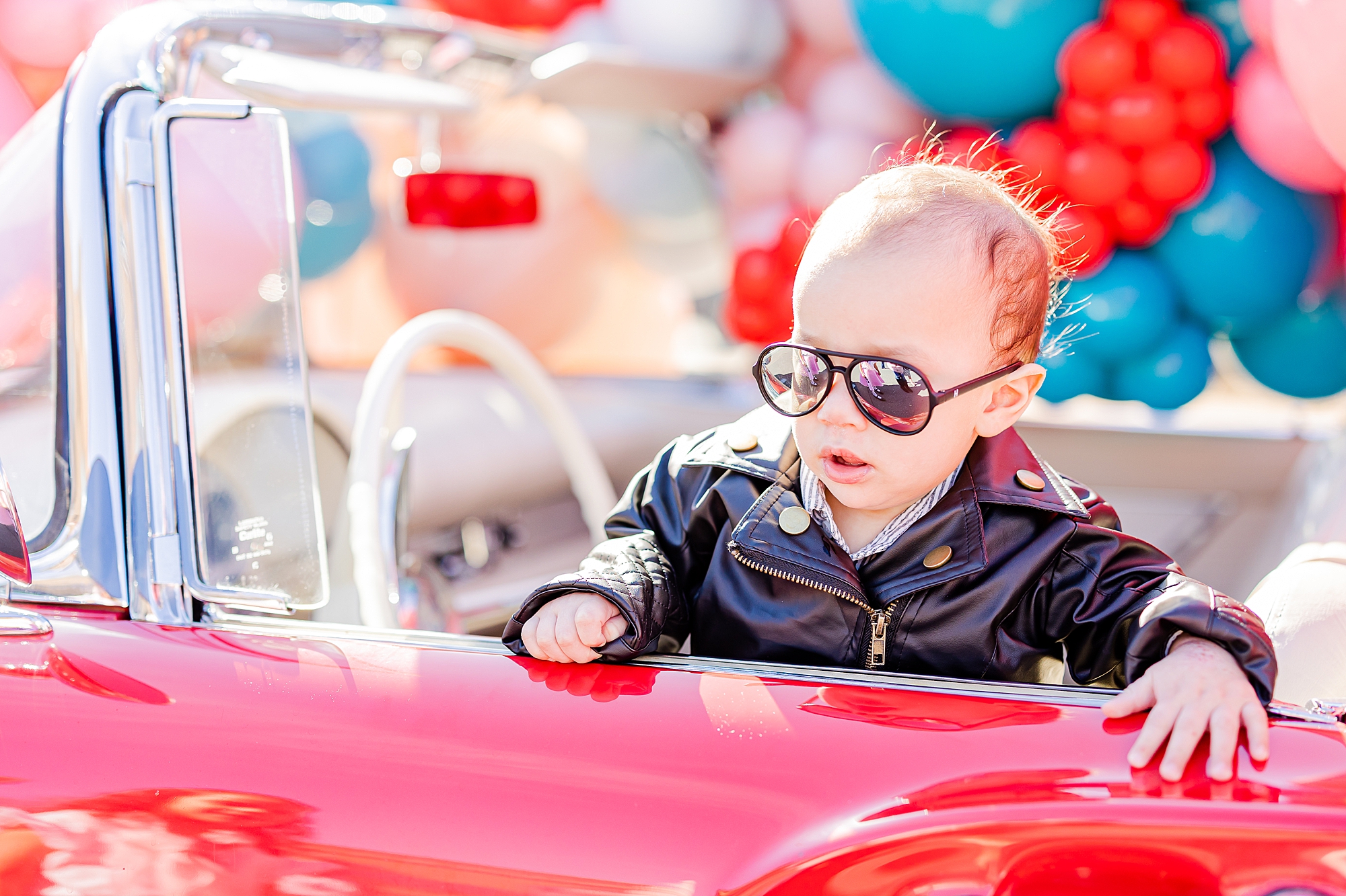toddler in leather jacket sits inside red Thunderbird 