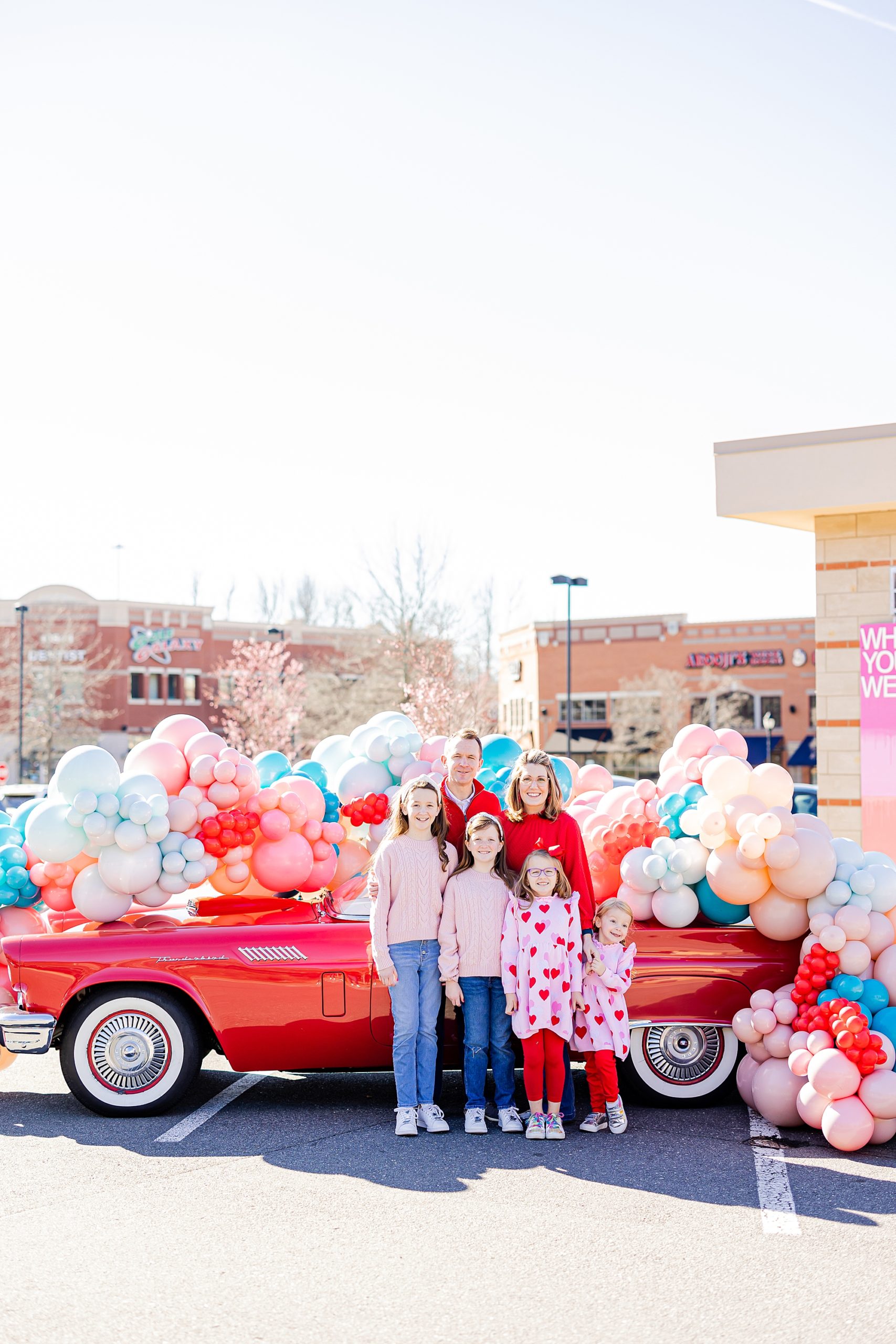 family poses by red thunderbird covered in balloons